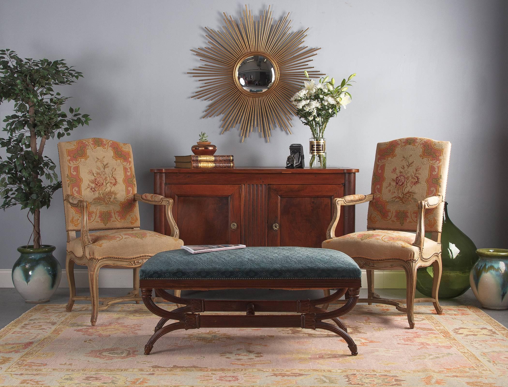 An ornate upholstered Spanish Savonarola bench in carved walnut, circa 1920. Walnut base with original velvet upholstery over spring seat. The base has an elongated Savonarola X-form shape with carved ribbing around the bottom of the seat and along