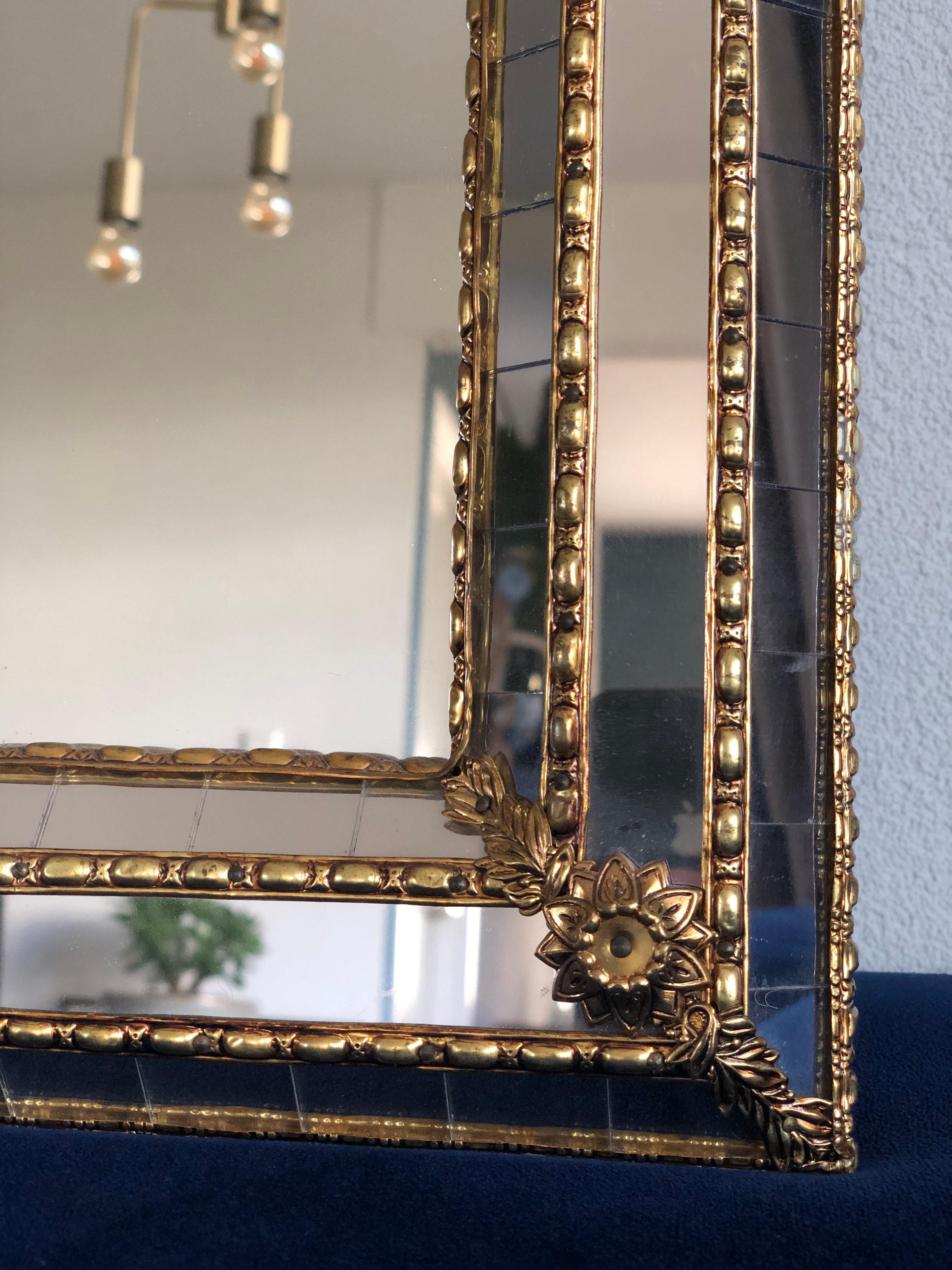 Beautiful handmade Venetian mirror from Spain 1990s. The frame with an arch at the top
has cut glass panes across the entire width, which is held together by a brass strip. The flawless mosaic trapezoidal mirror has a brass flower at each corner.