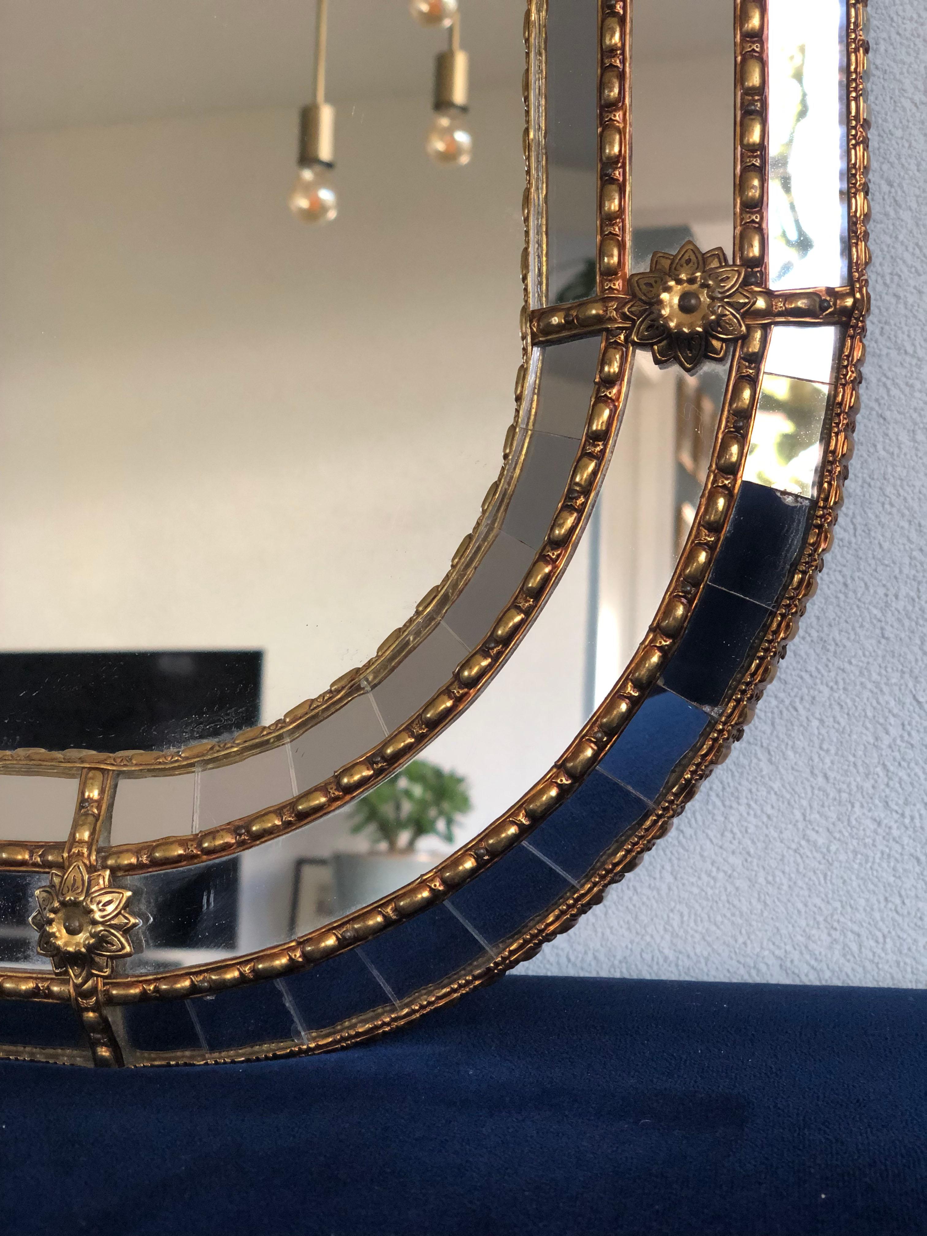 Beautiful handmade Venetian mirror from Spain, 1990s. The frame with oval corners has cut glass panes across the entire width, which is held together by a brass strip. The mosaic trapezoidal mirror has a brass flower at each corner. 

Object: