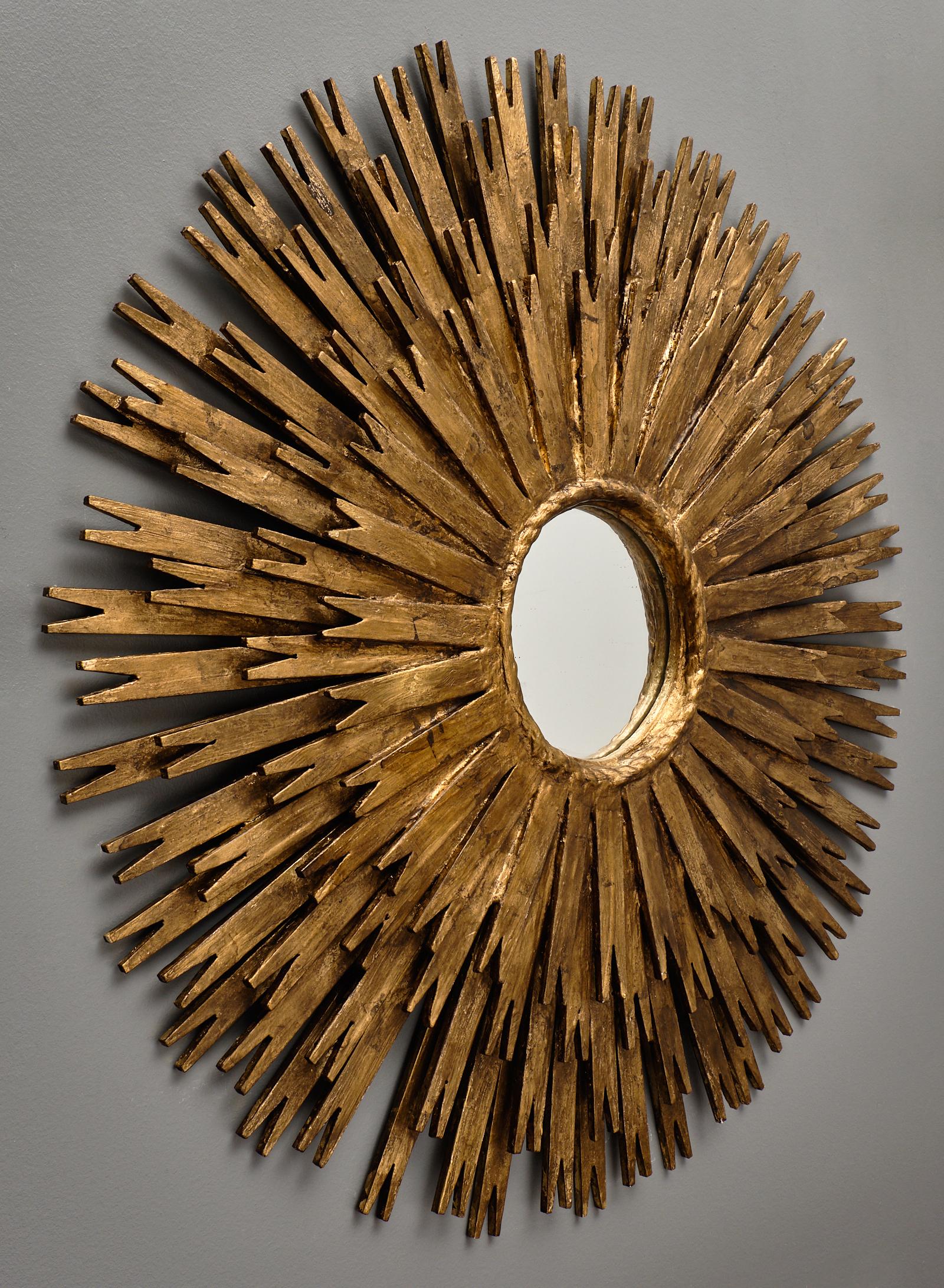 A vintage Spanish sunburst mirror featuring layers of hand carved and gold-leafed wooden rays. The round center mirror is framed by a twisted rope texture from which the rays originate.
