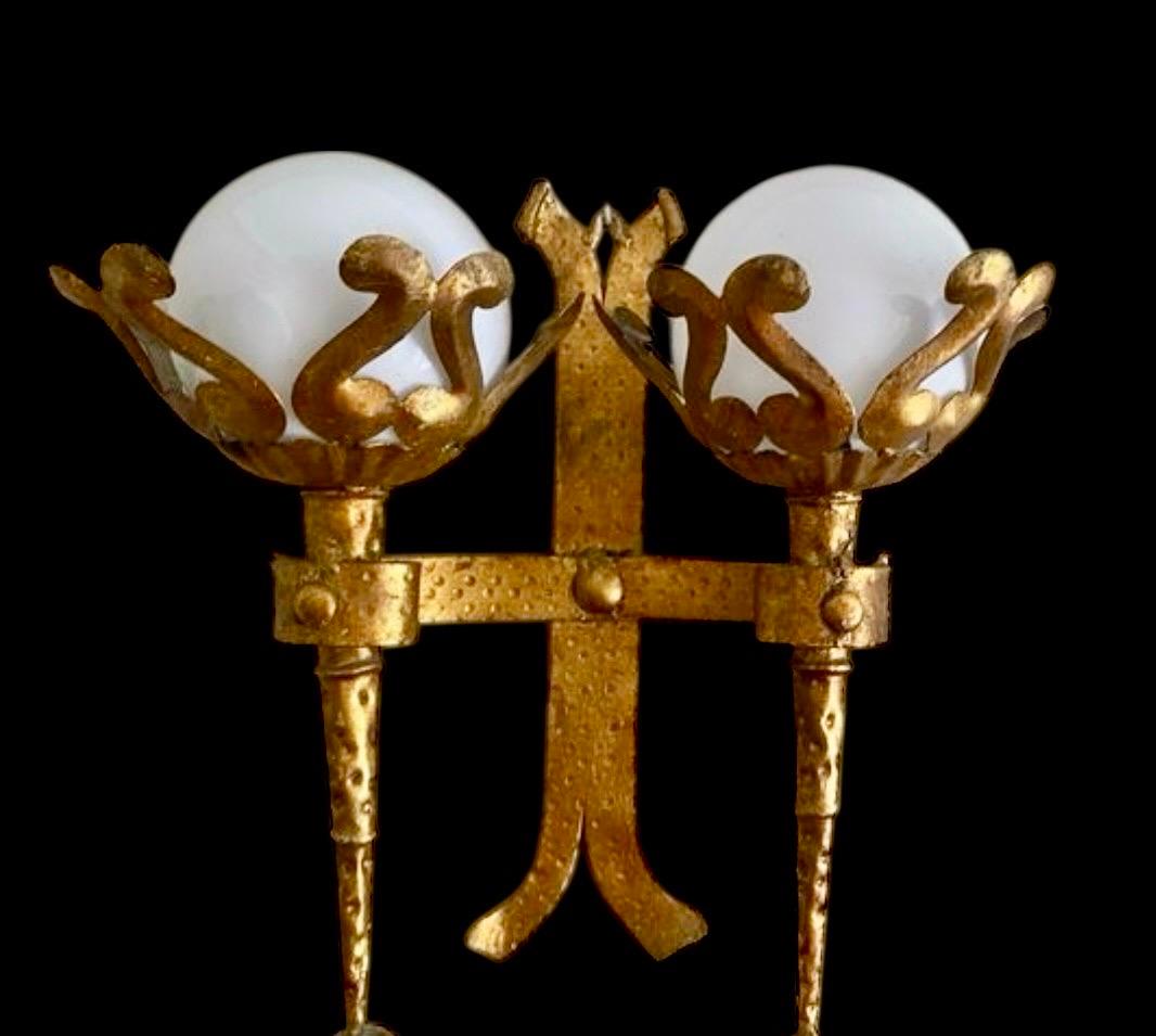 Applique gotica revival in ferro battuto dorato a foglia d'oro con due paralumi a globo in vetro opalino, Spagna, anni '50.
Questa torcia da parete è realizzata in ferro battuto a mano. È riccamente ornata dai segni del martello e rifinita con una