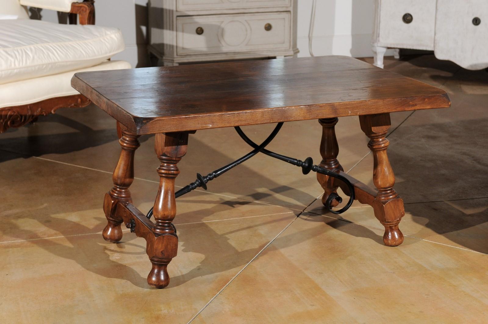 A Spanish walnut Fratino style coffee table from the 20th century, with iron stretcher and turned legs. This Spanish walnut coffee table features a rectangular planked top with beveled corners, sitting above an exquisite base. Four splayed turned