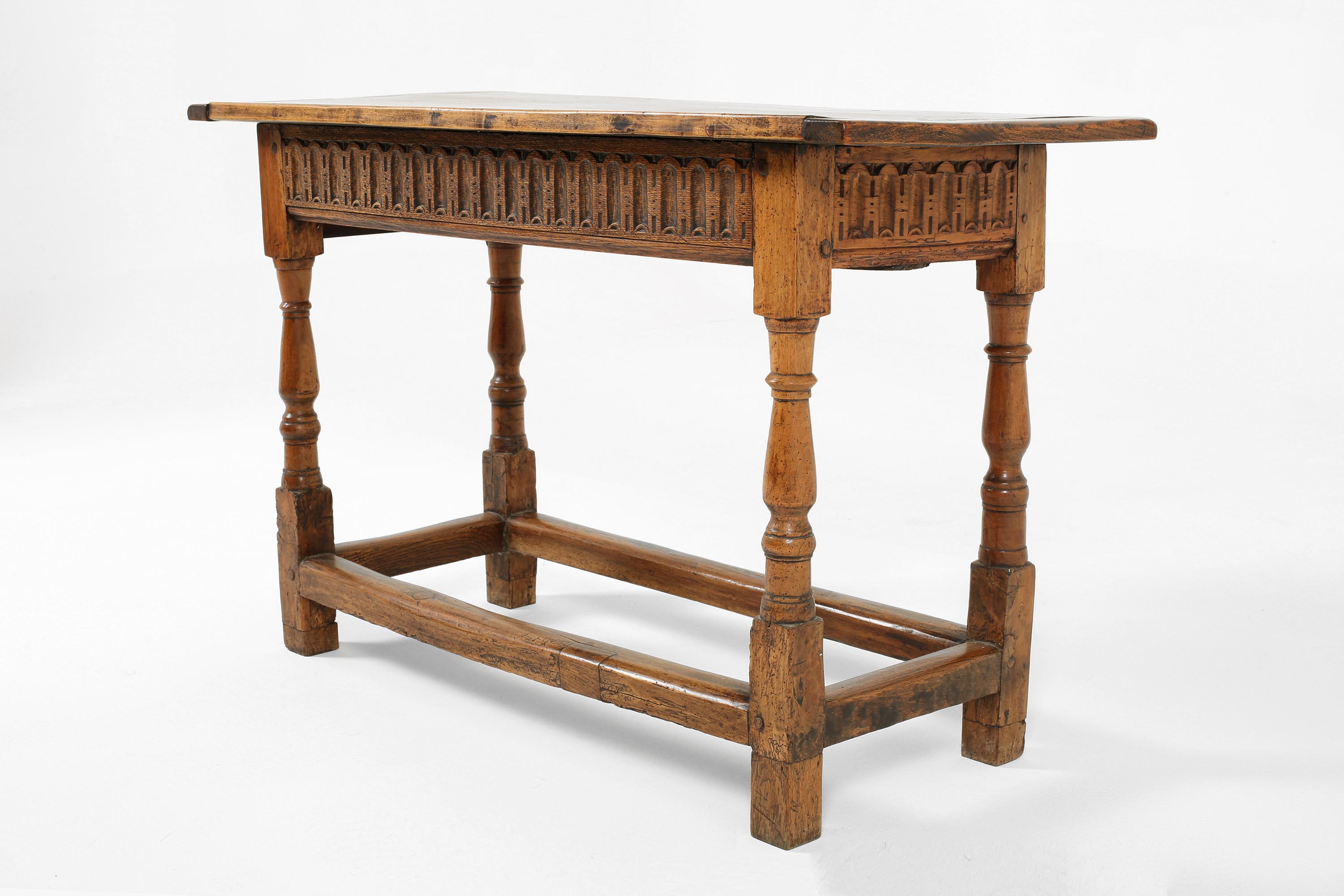 A walnut and oak console or lamp table with a decorative carved frieze, turned legs and a two plank top with cleated ends. Spanish, 17th century with some later elements.