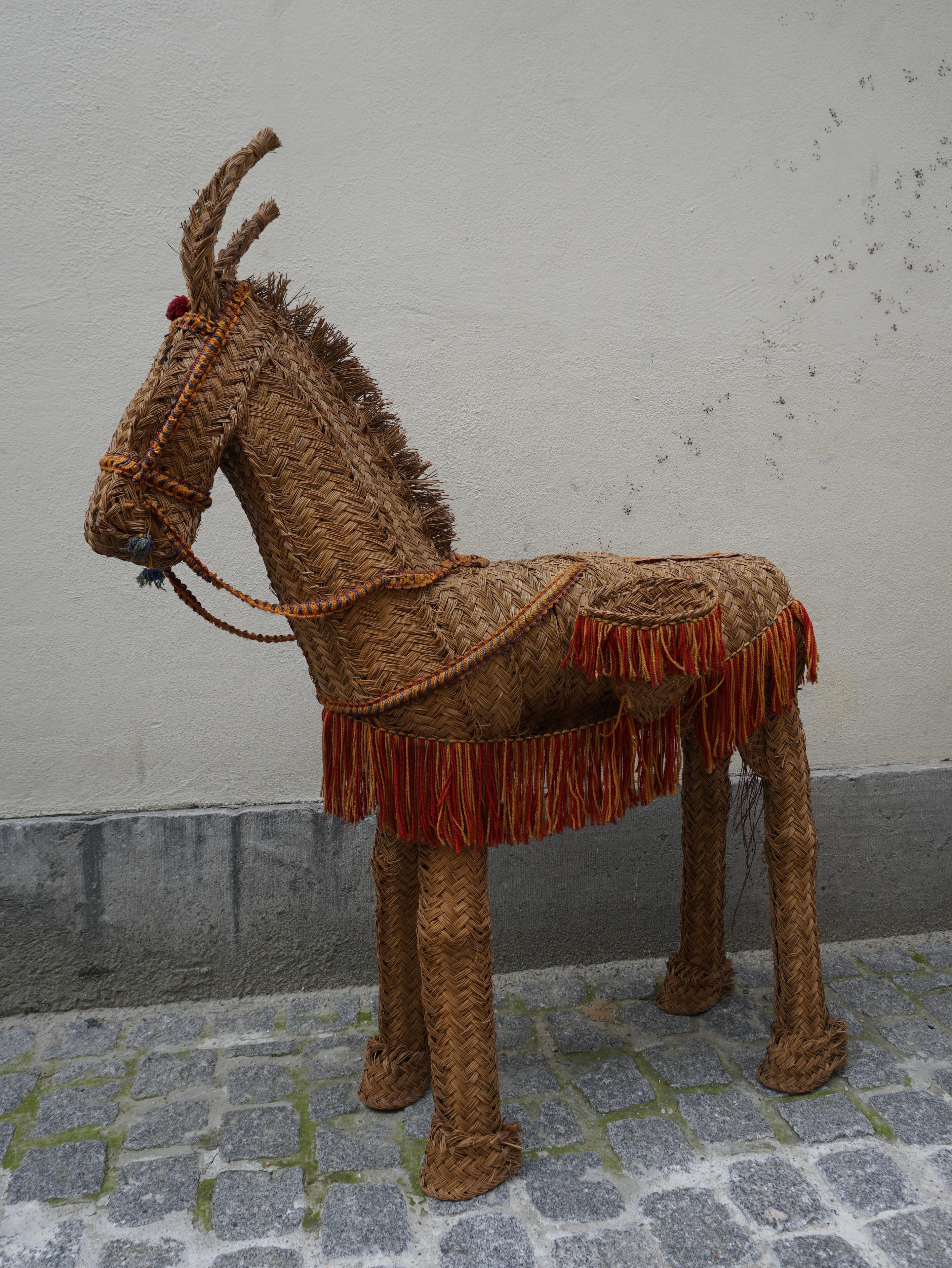 A decorative wicker donkey from Spain, circa 1950s.An artisan piece with a rustic, Mediterranean feel. Wicker side baskets evoke goods sold at a market or roadside, while decorative fringe adds a carnival touch of color. The jaunty tilt of the ears