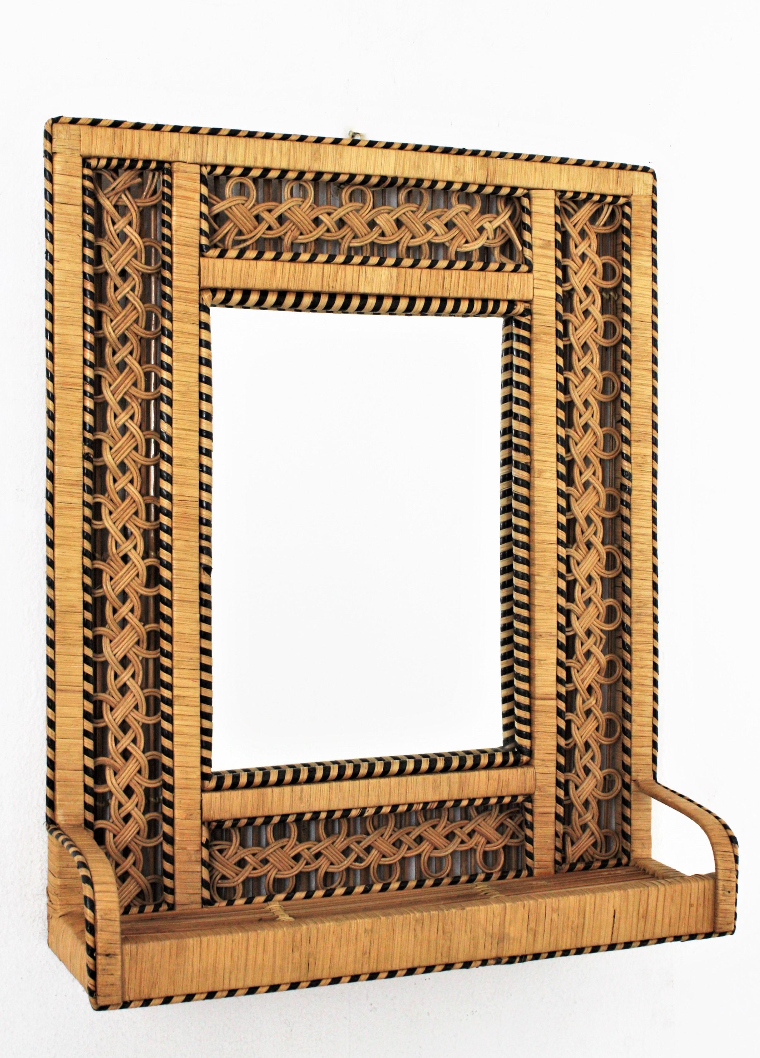 Lovely Bohemian style handwoven rattan and wicker rectangular mirror with shelf, Spain, circa 1960-1970s.
The braided frame was handcrafted in the manner of the Emmanuelle Peacock chair. It has a meticulous handcrafted woven work with black accents