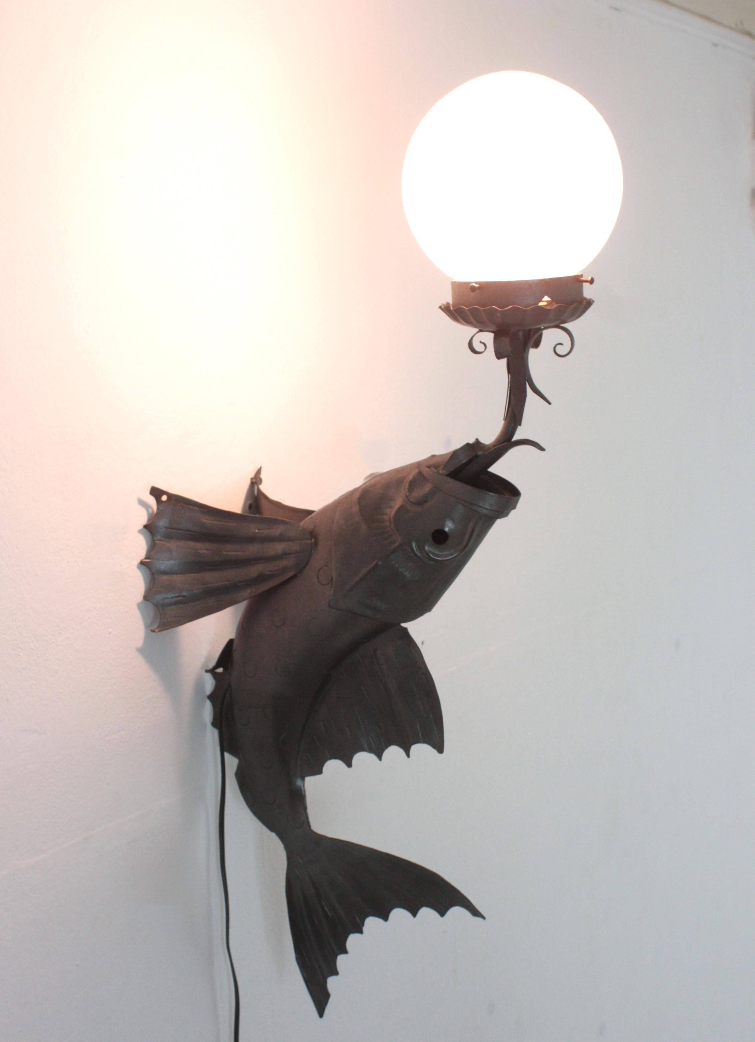 Wrought Iron Fishe Wall Light with Frosted Glass Globe Shade. Spain, 1950s-1960s
Rare find.
This single light wall sconce was handcrafted in Spain at the Mid-Century Modern period in the style of Brutalism. 
It features a large iron fish blowing