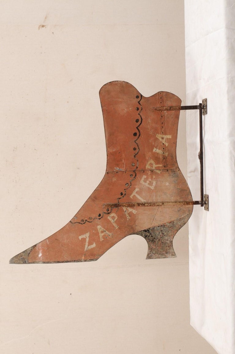 A Spanish shoe storefront sign from the mid-20th century. This vintage shop sign from Spain is double sided metal, just into the shape of a ladies heeled boot. The sign is intended to be suspended from the wall using mounts found at top and bottom