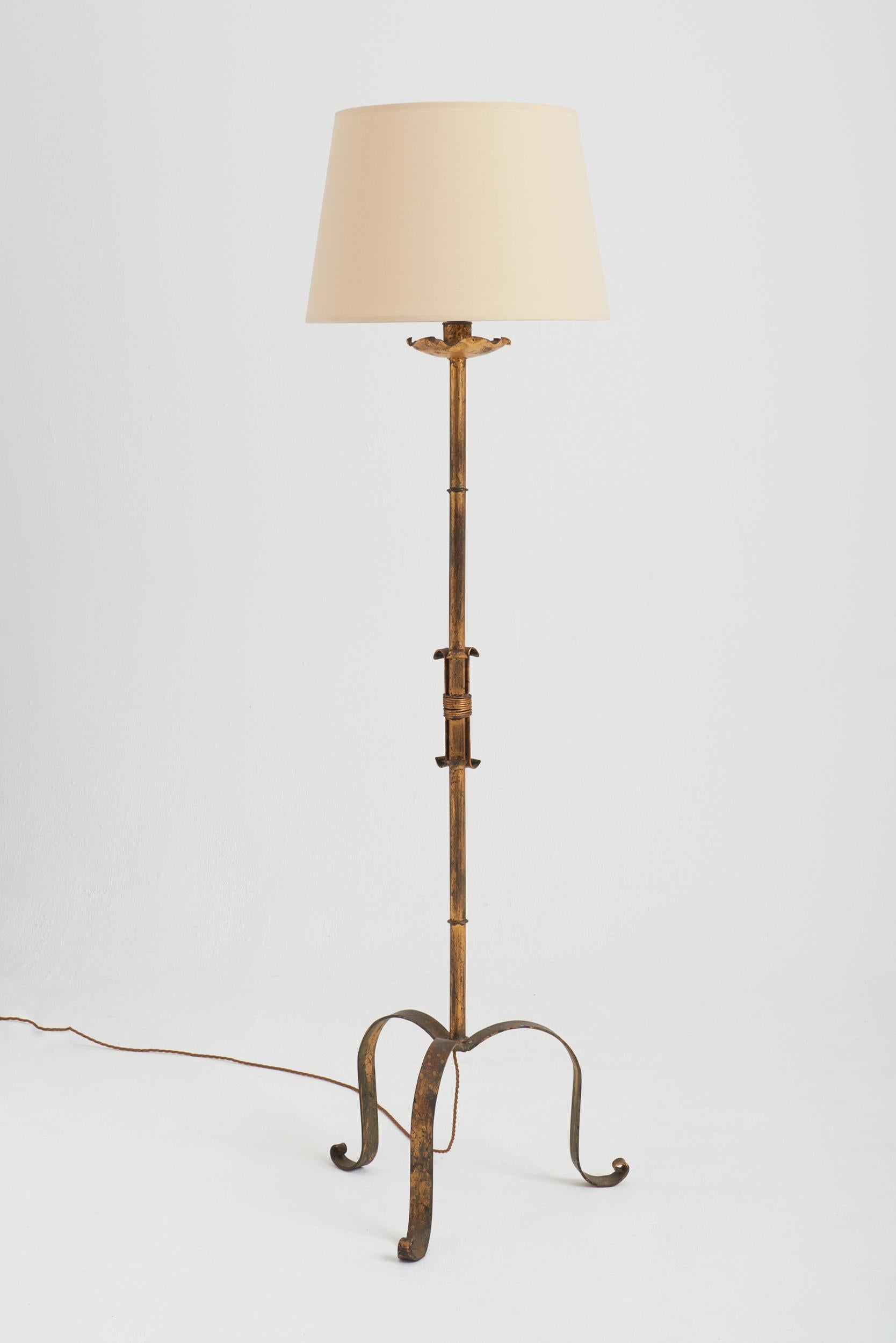 A gilt forged iron floor lamp.
Spain, third quarter of the 20th century.
Measures: With the shade: 167 cm high by 46 cm diameter. 
Lamp base only: 143 cm high by 50 cm diameter.