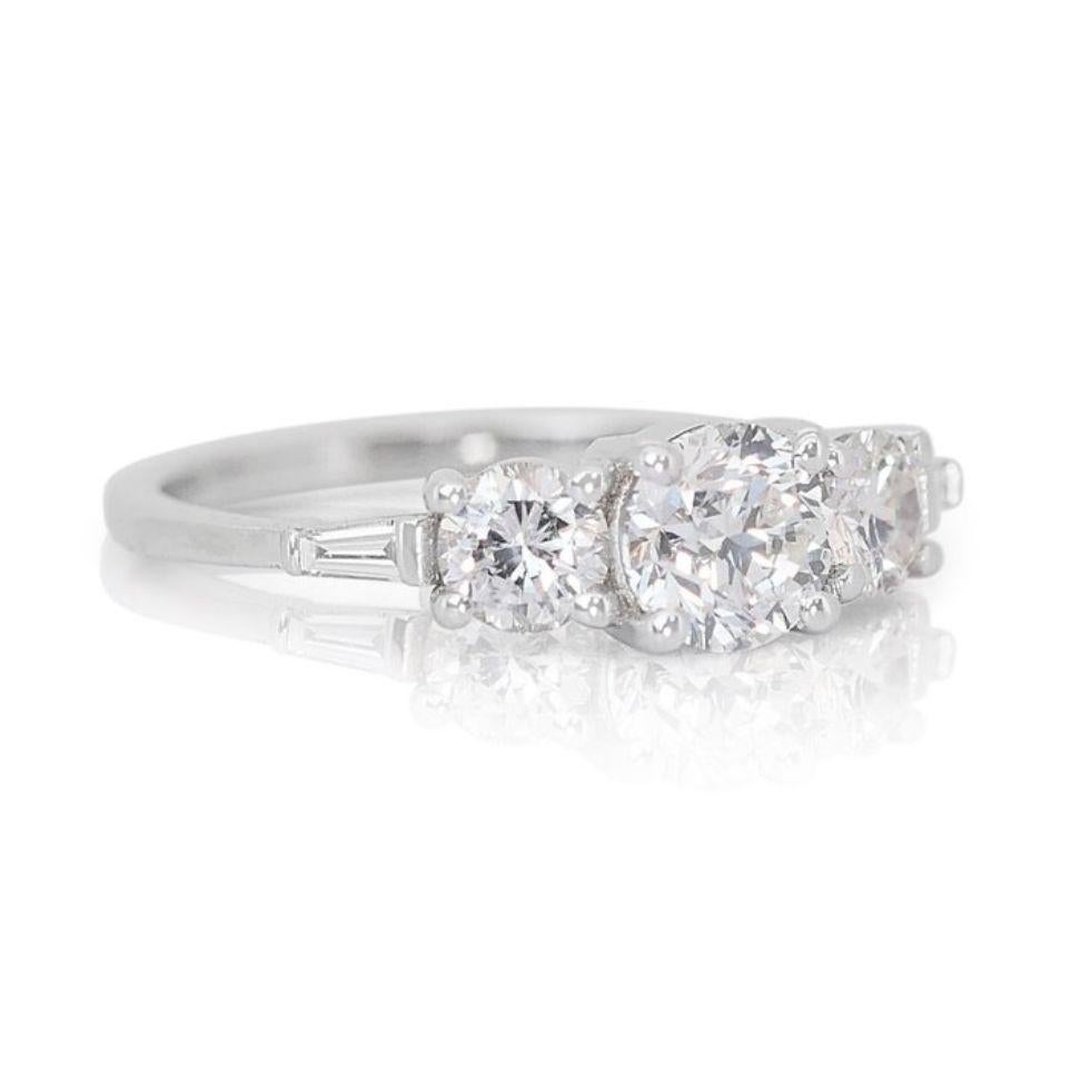 This captivating ring showcases a central round brilliant diamond weighing 0.7 carats, captivating your gaze with its brilliant F-G color and mesmerizing VS2-SI1 clarity. Its vibrant sparkle is accentuated by two tapered baguette diamonds (totaling