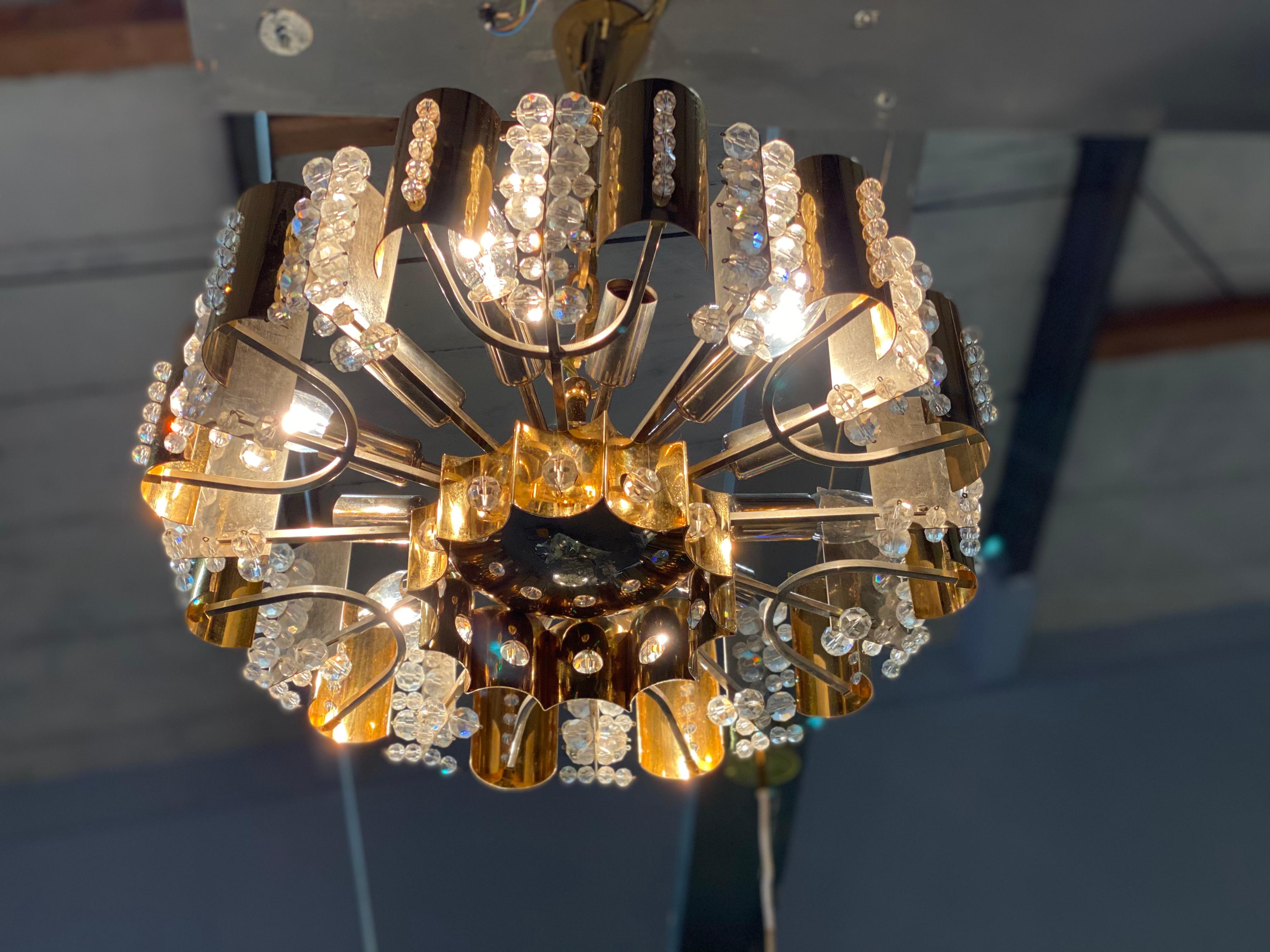 This gilded brass chandelier with its design and many crystal stones can be attributed to the manufacturer Palwa and the 1960s.

Palwa is composed of the names Palme and Walter. The company was founded by two German families and grew rapidly in