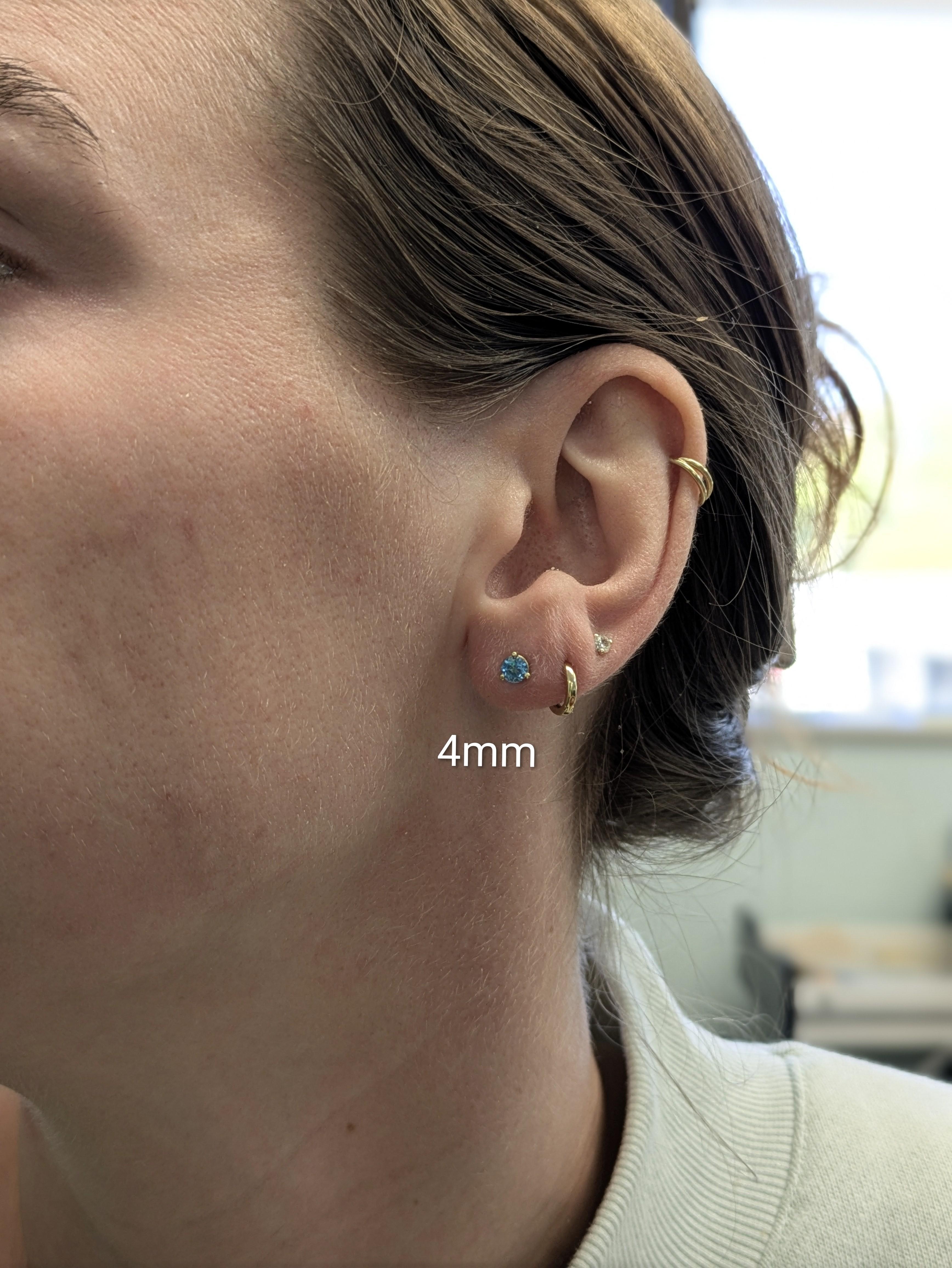 Eleganti orecchini a perno in oro massiccio 14k con gemme rotonde brillanti di topazio azzurro da 4 mm. La loro scintillante tonalità celeste aggiunge un tocco di raffinatezza senza tempo a qualsiasi look.


