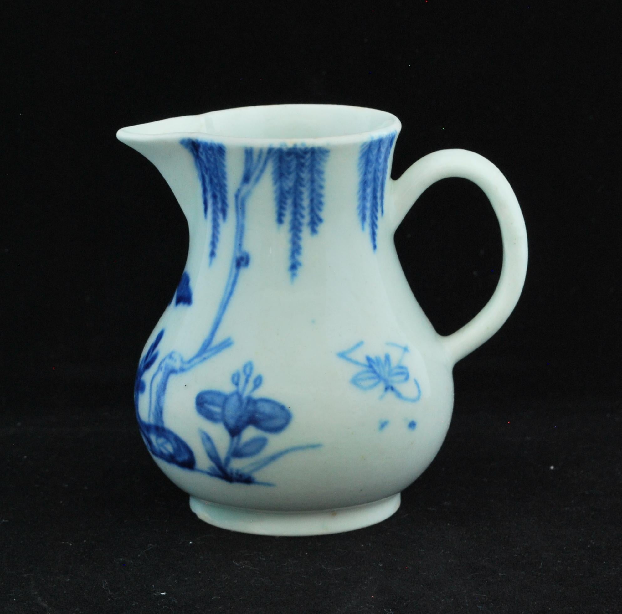 An early, small baluster jug with high foot rim, loop handle and ‘sparrow beak’ lip. Potted in a dense white body, slightly iridescent silky glaze, and painted in blue underglaze with rocks, flowering plants and a willow; an insect at each side of