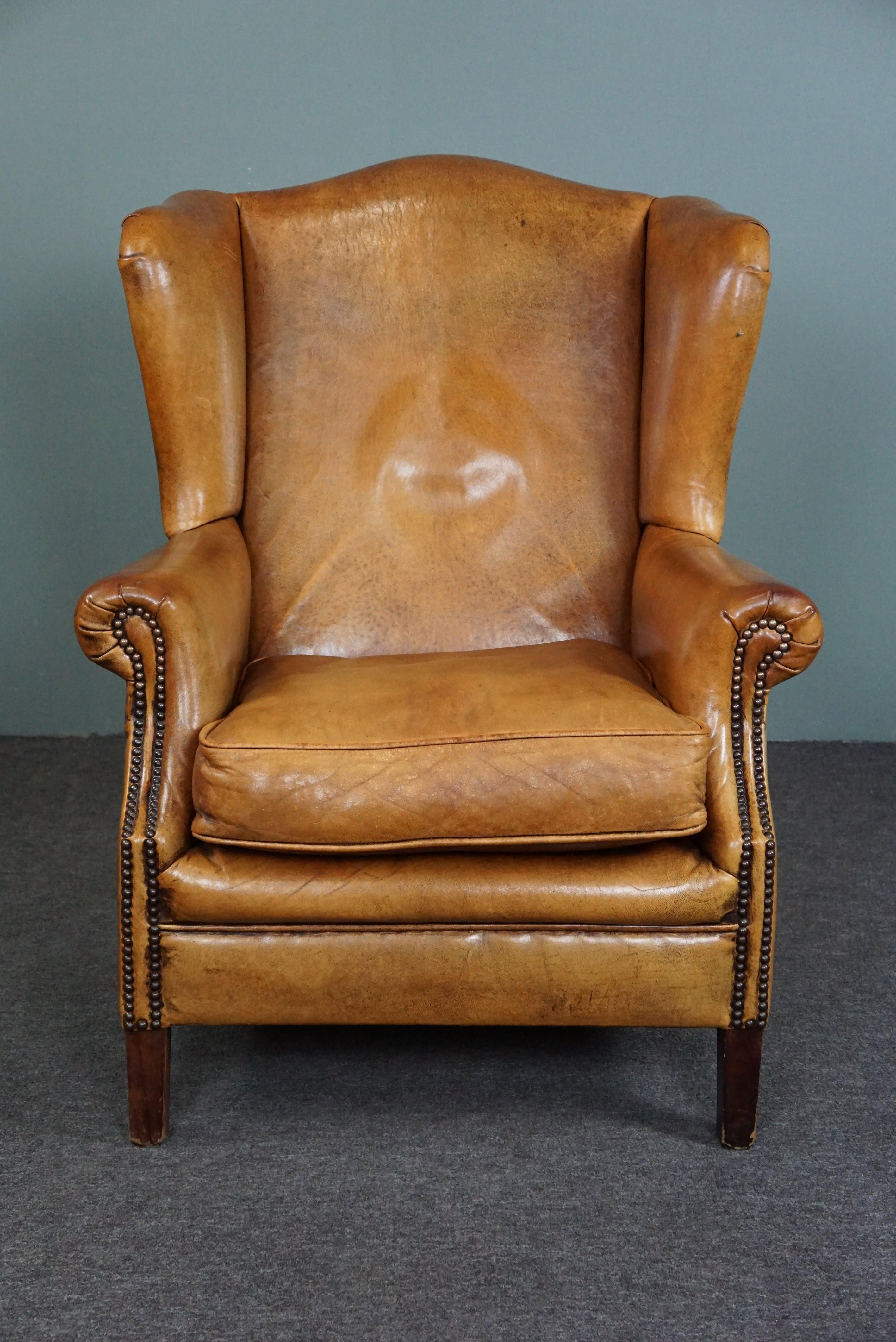 Offered is this beautiful warm-colored sheep leather wing chair finished with wooden legs and beautiful decorative nails.

This pearl has an unsurpassed expressive color with a beautiful patina.
Anyone who takes this unique eye-catcher into their