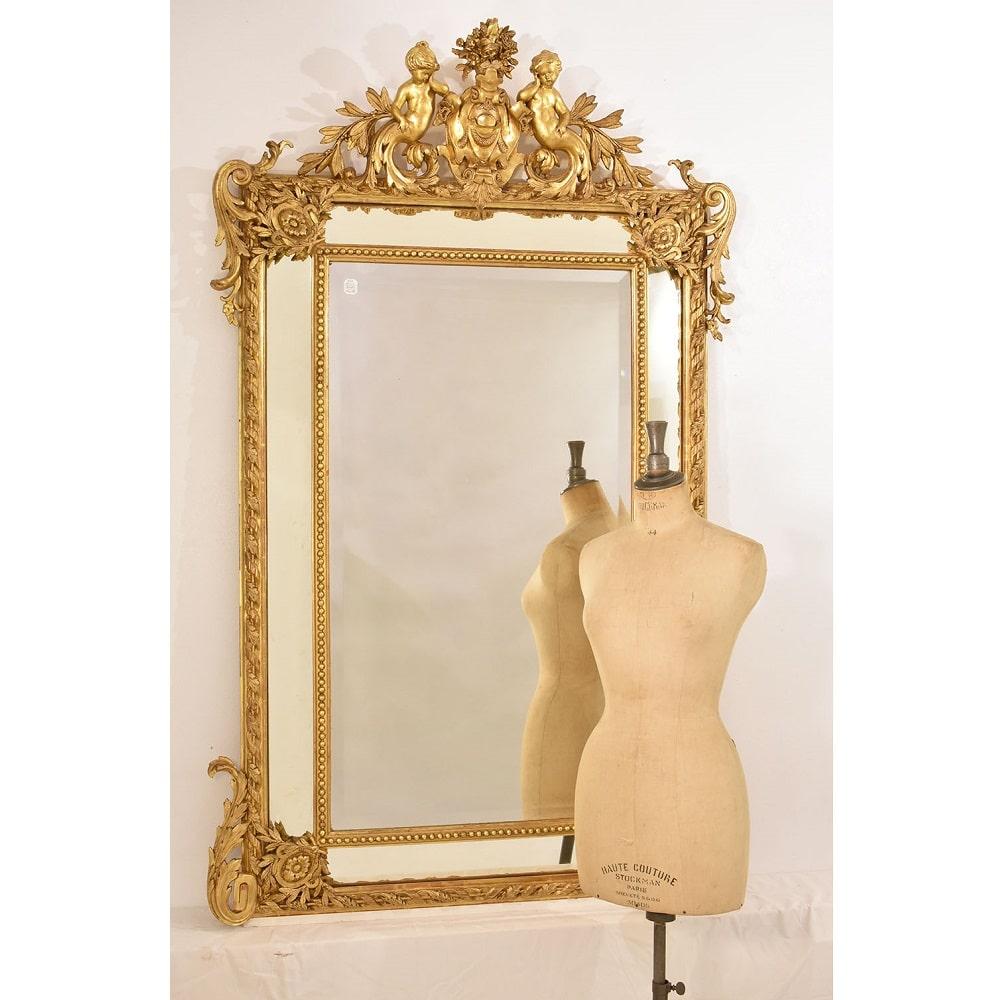 L'elegante e bella Specchiera Antica Con Cimasa ricca di Volute e Con Putti qui proposta risale al XIX Secolo.

Lo specchio antico centrale è molato di epoca Ottocento. La Doratura Originale è di ottima qualità.

Cornice Dorata In Foglia Oro