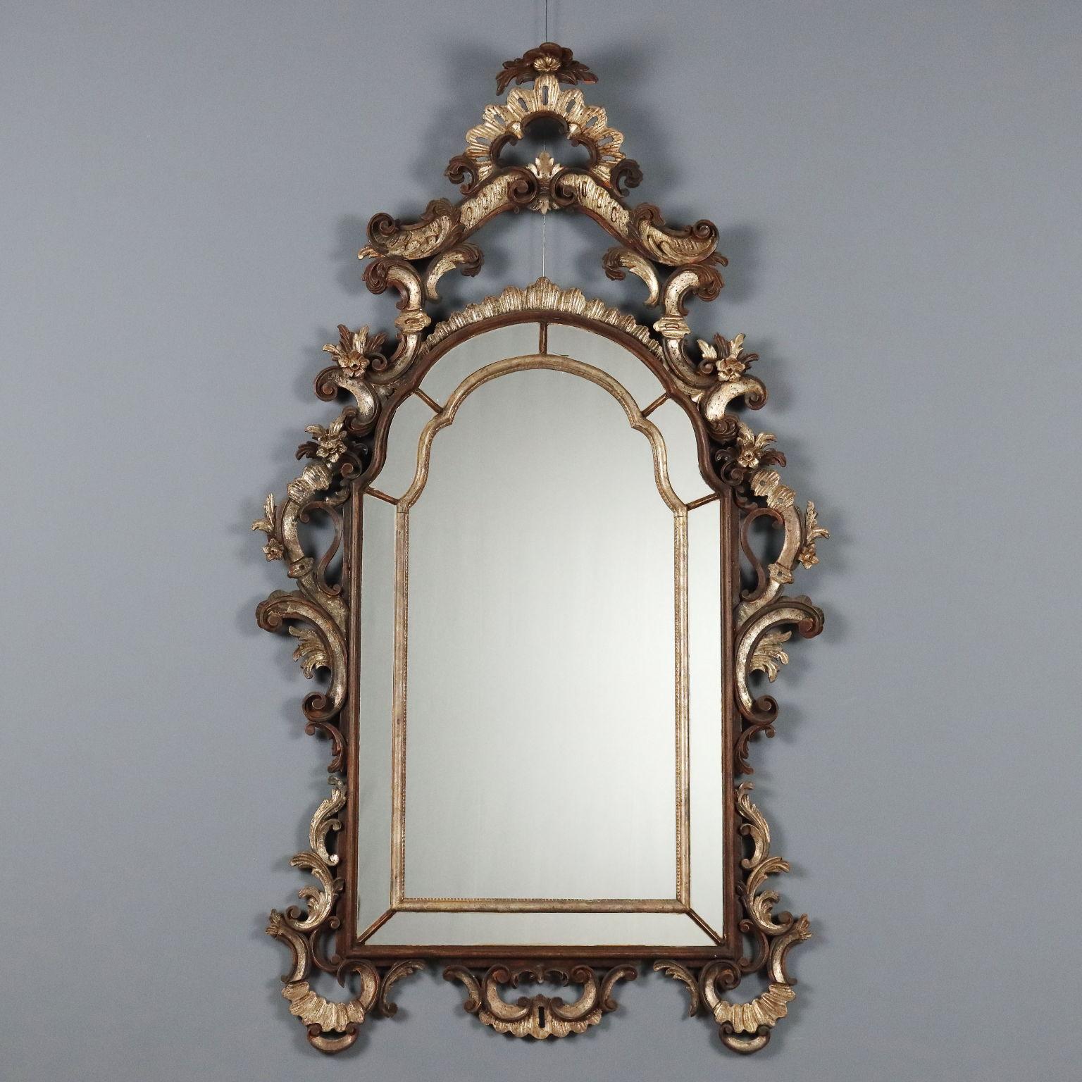 Espejo de estilo rococó, lacado y pintado. Espejo central rodeado de un grupo de espejos, marco de madera calada con tallas rocaille de roleos, rizos y flores.
Italia, primera mitad del siglo XX.