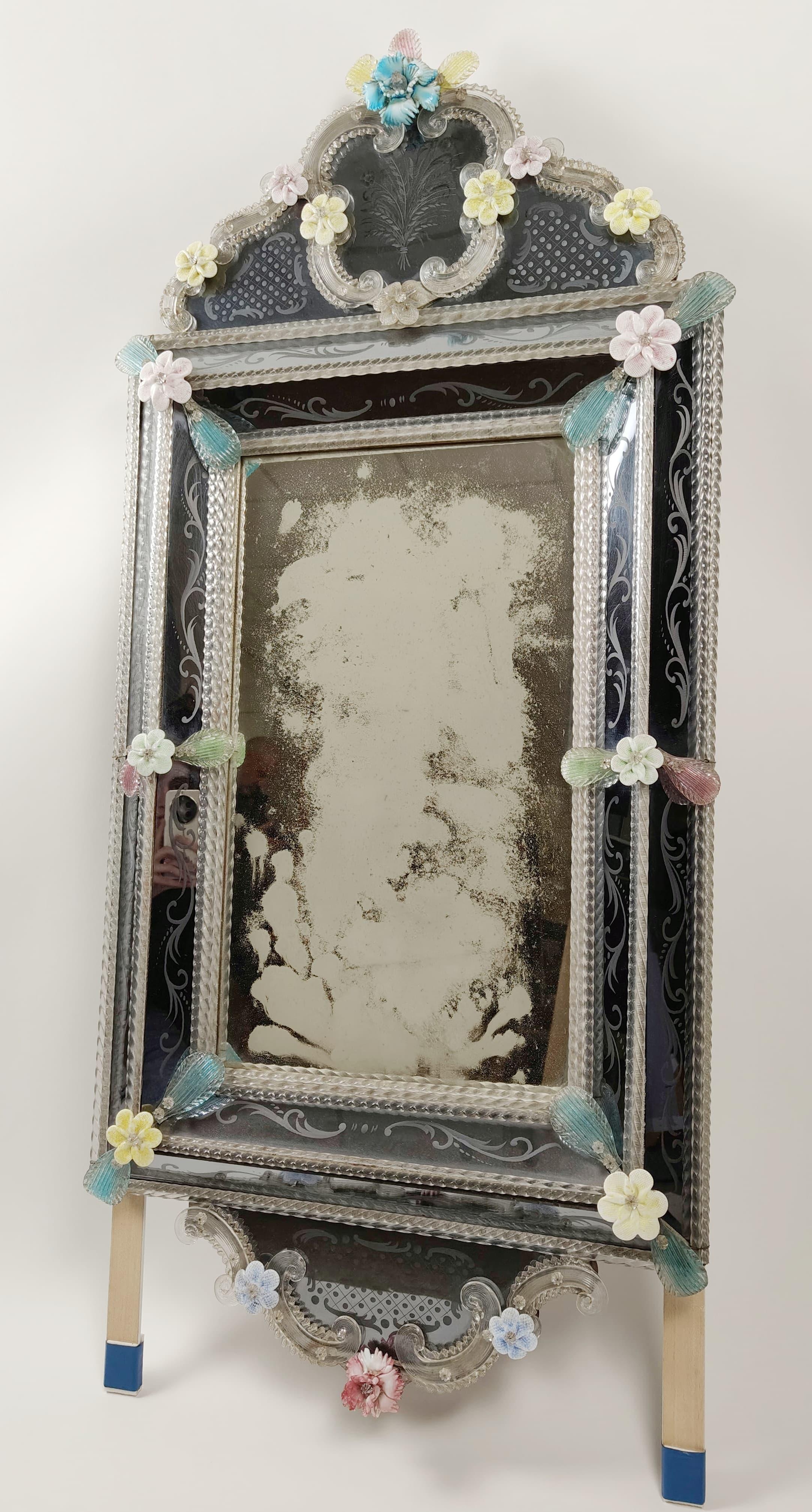 Miroir réalisé dans les années 1950 en verre de Murano, avec des applications florales décoratives, également en verre de Murano, de différentes couleurs. Le cadre comporte une décoration florale gravée supplémentaire.
Travaillé et produit par des