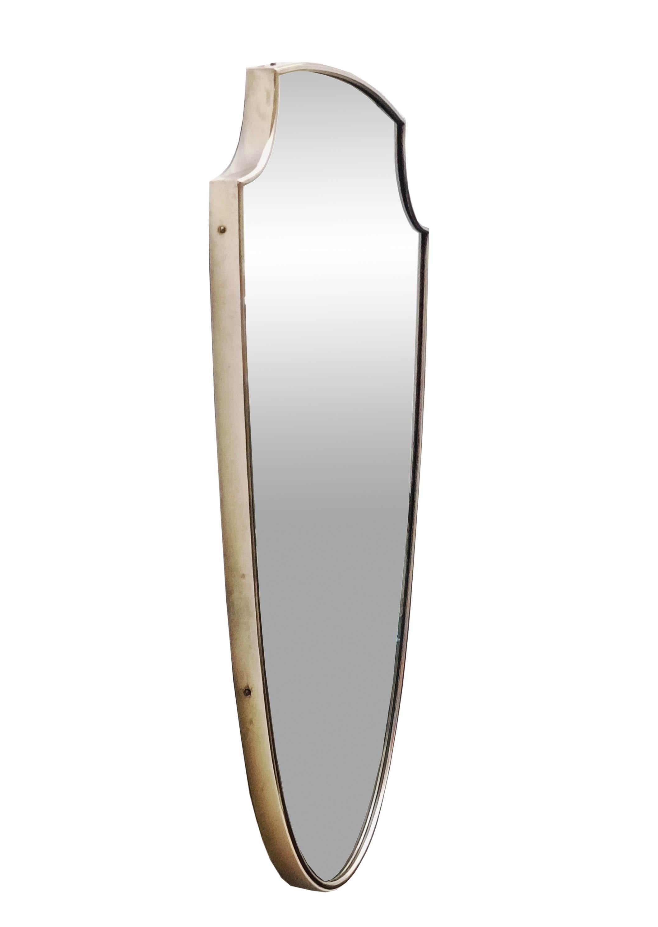 Solid brass shield wall mirror made in Italy in the 1950s in the manner of Giò Ponti, The frame is in good overall condition with an aged patina; on the mirror glass are some small   period imperfections. 