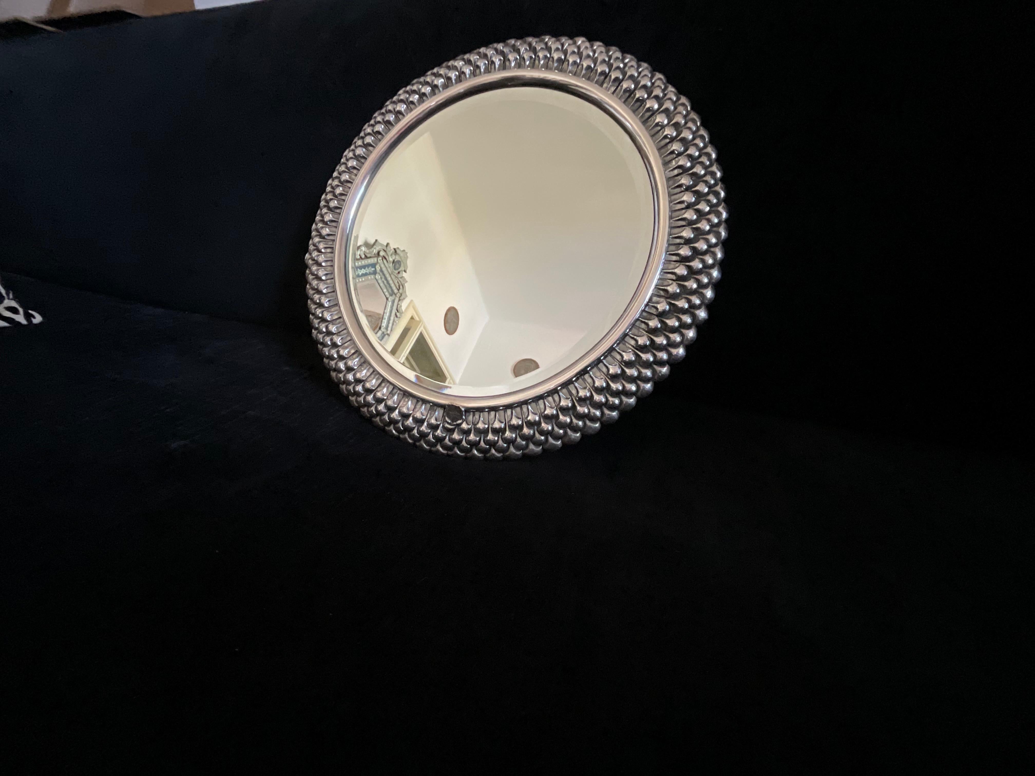 Una bellissima specchiera da appendere con la cornice in argento 925 (PUNZONE) è ha uno stemma con una firma probabilmente di chi l’ha fatta, ma purtroppo non leggibile bene. 
Comunque ha una lavorazione a sbalzo di ottima qualità.