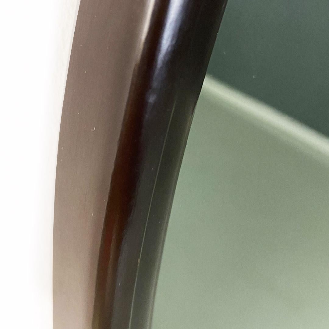 Specchio da parete di forma tonda, di medie dimensioni con cornice in legno di colore marrone scuro, con unico dettaglio di lavorazione presente nella parte alta e interna della cornice, che per tutto il perimetro resta regolare ed uniforme. Vetro