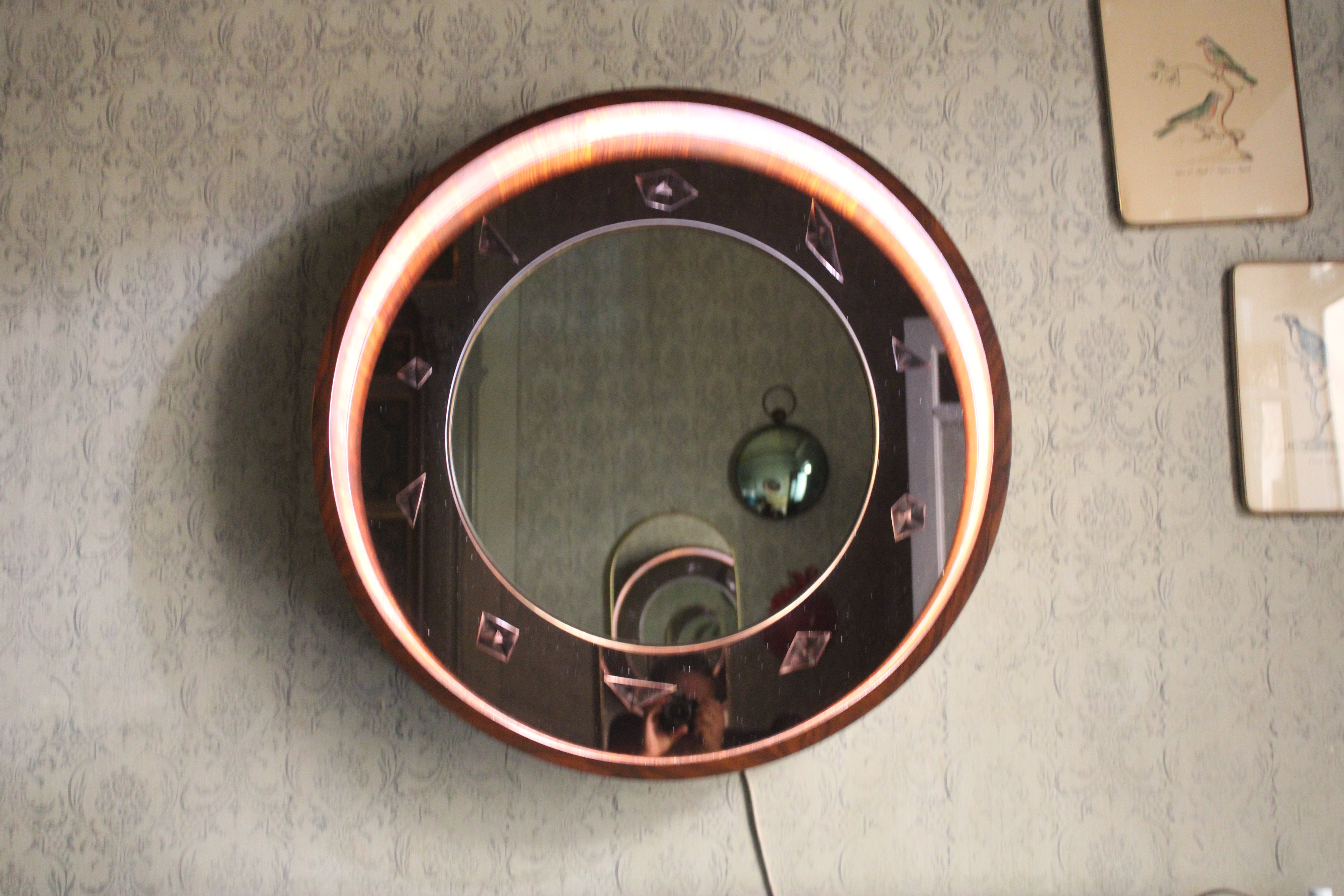 Raro espejo retroiluminado con marco circular de madera dentro de espejo con marco de latón y fondo de cristal coloreado con motivos geométricos, un objeto raro y muy elegante de los años 50 en Italia. El mismo fue vendido en una famosa subasta