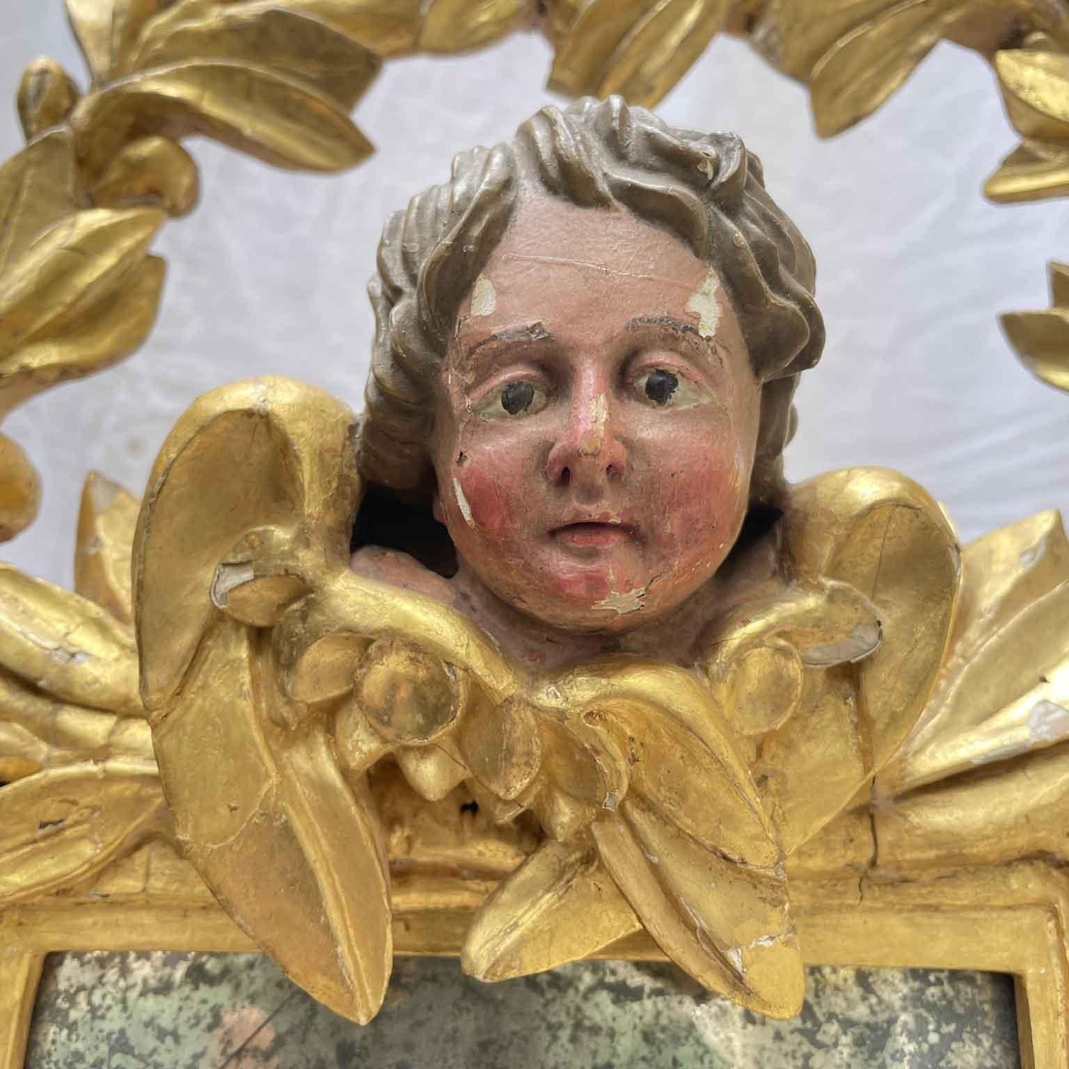 Italian Gilded Mirror With Putto in Baroque style but from the early 1800s with the square-shaped frame surmounted by the head of a winged putto framed by a rich garland of laurel leaves that also run down the sides of the frame.  The decoration