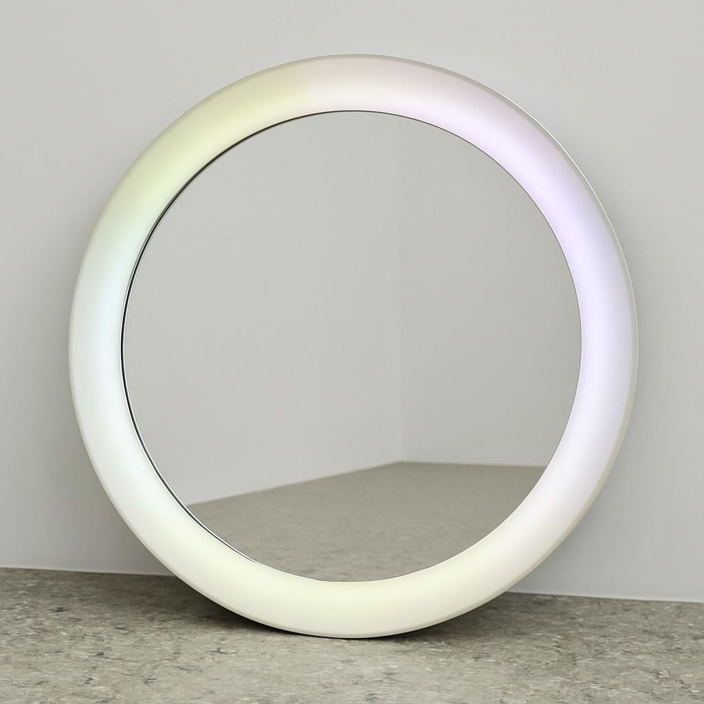 Iconico specchio rotondo dal design Space Age, originale degli anni ’70, con cornice in plastica satinata che integra una retroilluminazione a gradiente, dai toni pastello tenui (bianco, lilla, giallo chiaro). Il bordo ampio e bombato richiama lo