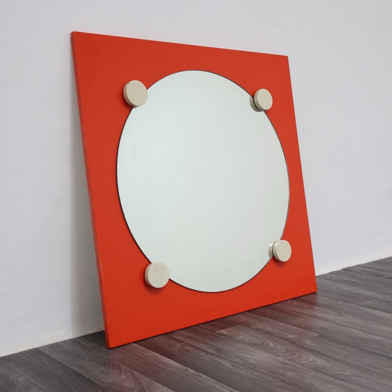 Specchio da parete dal forte impatto scenico, realizzato in legno laccato arancio con inserto circolare in vetro e dettagli geometrici in rilievo. Un pezzo iconico del design Space Age anni '70, caratterizzato da linee essenziali e dal contrasto