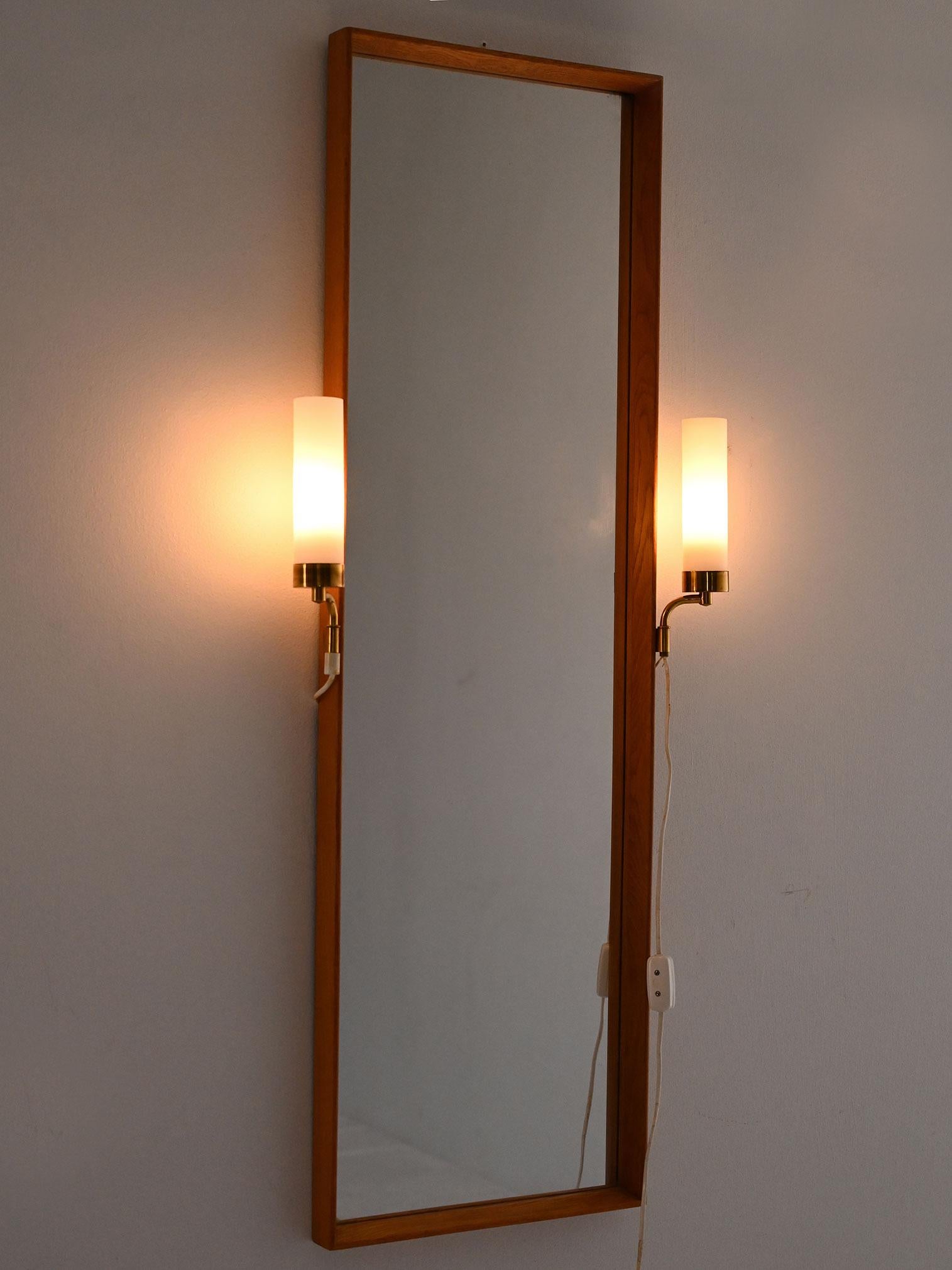 Espejo rectangular escandinavo de los años 50 con dos lámparas laterales de latón y cristal opalino, instalación original en funcionamiento.

Espejo escandinavo vintage de los años 50 con marco de madera y dos lámparas laterales integradas. Los
