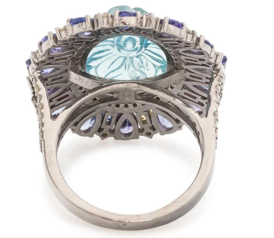 This captivating multigem and diamond ring is a testament to exquisite craftsmanship and intricate design. The ring features a central oval carved aquamarine, measuring approximately 16.5x11.5mm, which serves as the focal point. Surrounding the