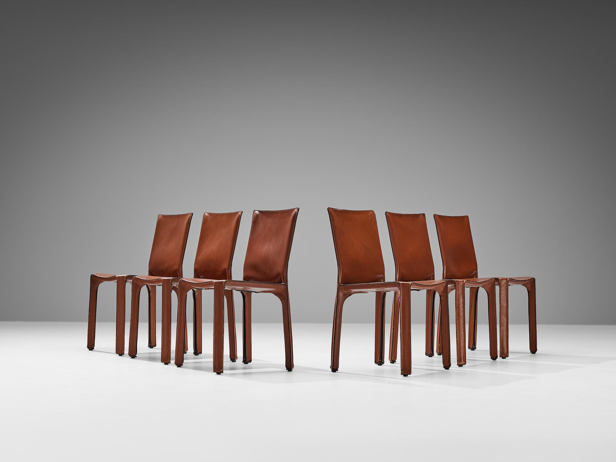 Beautiful set of six chairs in a rich red cognac leather designed by Mario Bellini. Conceptually, the chair was designed to become marked and shaped over time by its user. The leather skin fits like a glove over the steel skeleton fastened with four