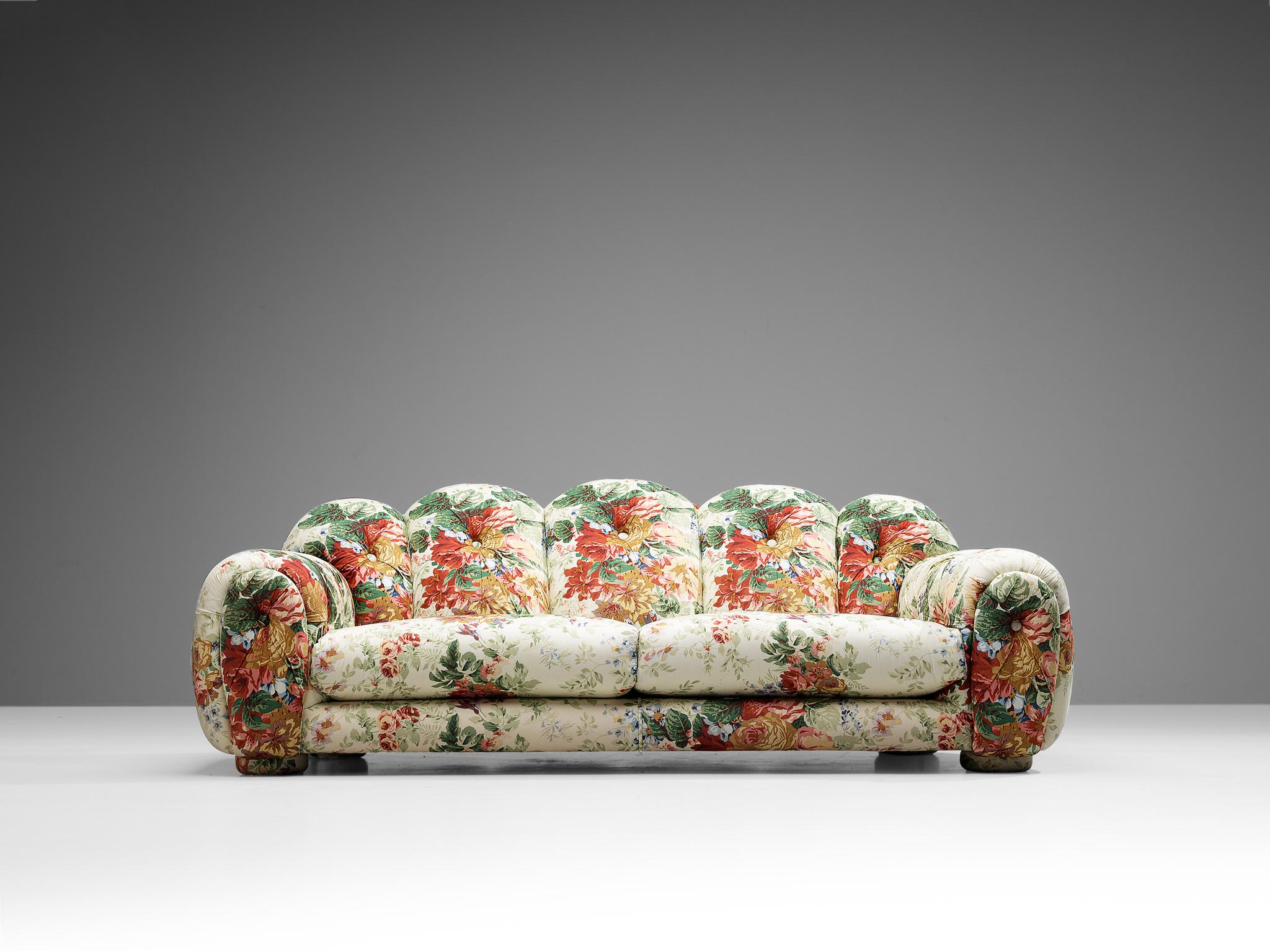 This vibrant and bulky sofa was manufactured in Italy in the 1970s. This item is upholstered in a multi tone tufted floral fabric. The smooth and bulky form, combined with the floral upholstery, creates a cheerful and cloud-like appearance. This