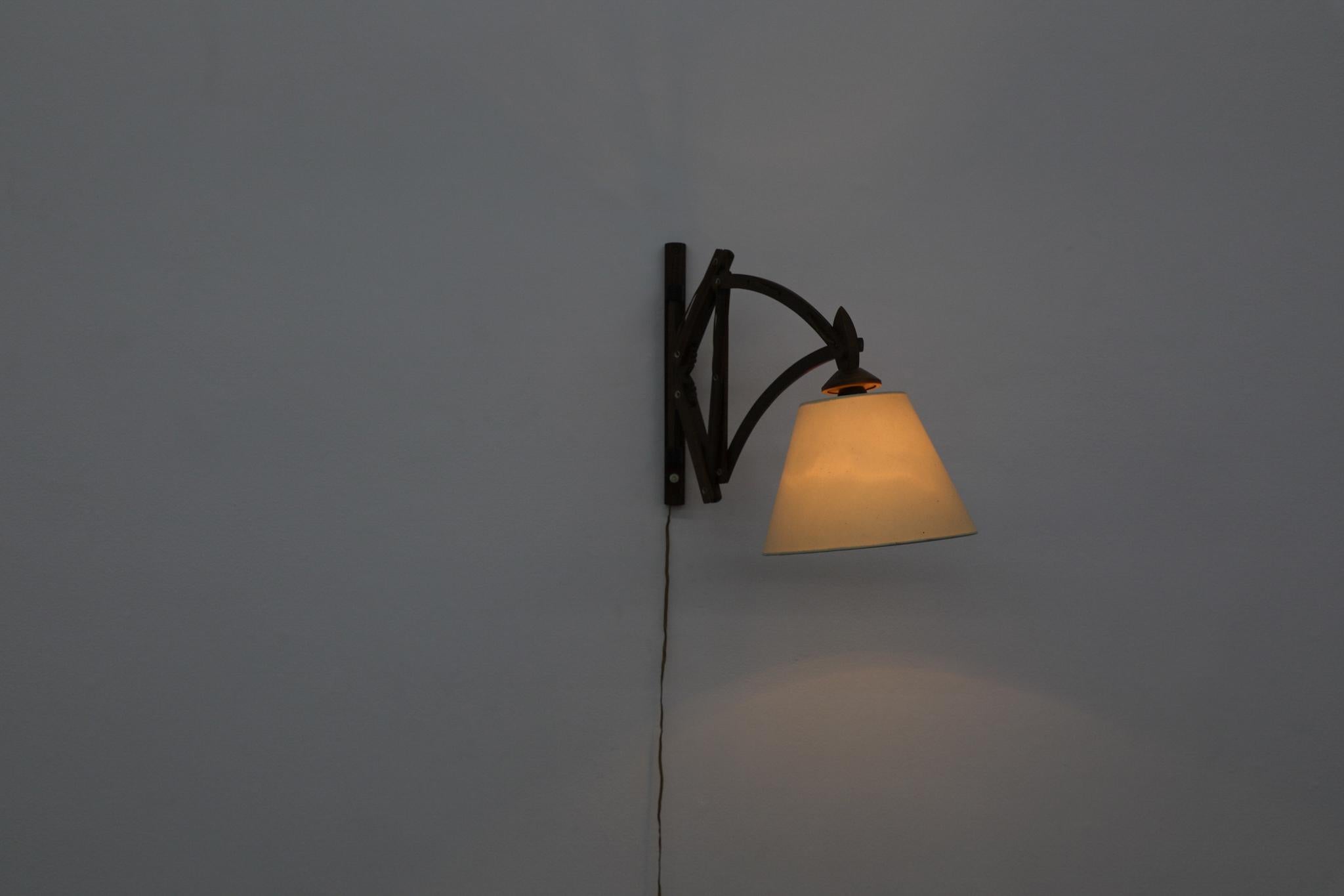 La lampada da parete a fisarmonica in teak di metà secolo combina un design funzionale con una calda estetica scandinava. Il meccanismo a forbice espandibile si estende dolcemente dalla parete, mentre il paralume conico in lino proietta una luce