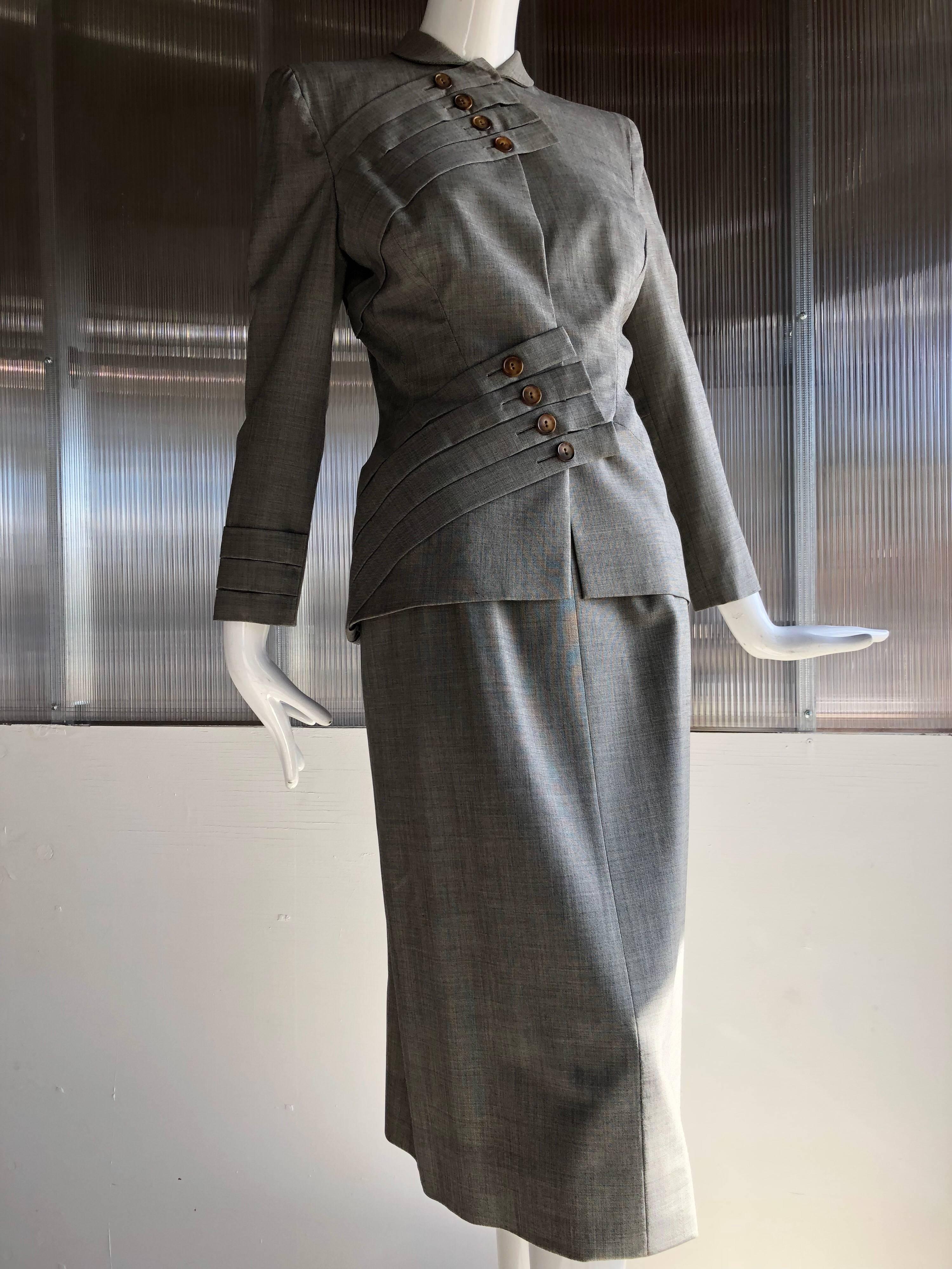 A spectacular 1940s Gilbert Adrian skirt suit created with typical Adrian panache!  Gray wool gabardine suiting is fashioned into a slew of button embellished straps that wrap over the bust on one side and the hip on the other.  Hidden hook and eye
