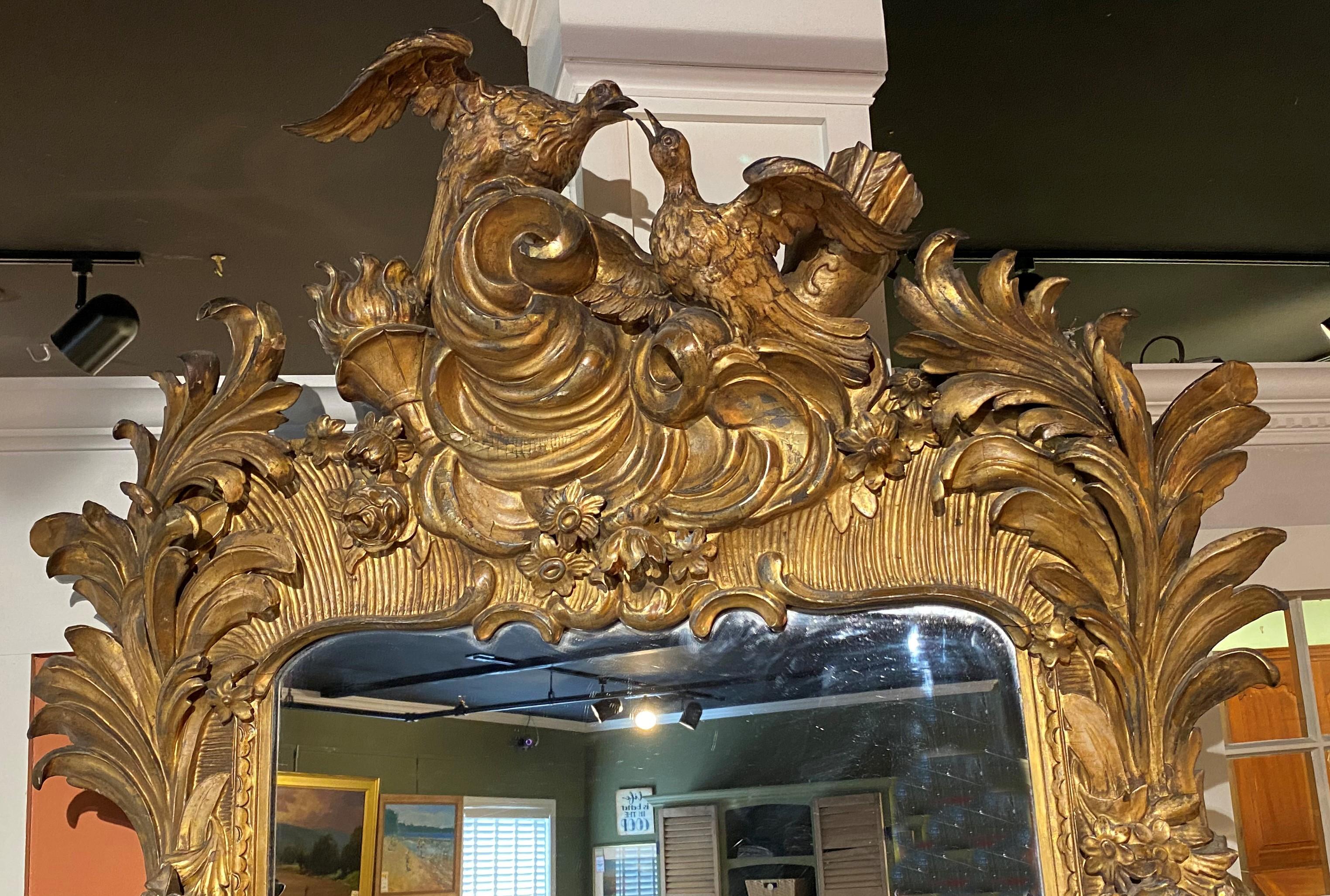 A spectacular Italian carved and giltwood Rococo rectangular pier mirror with an exceptional foliate carved frame and crest featuring two birds, a quiver with arrows, a flame torch, and large scrollwork accents. Comes with a matching giltwood
