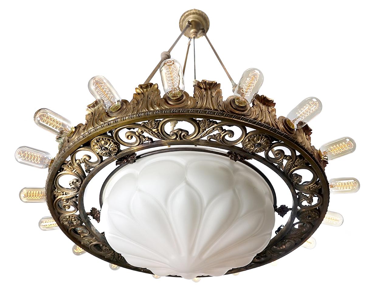This monumental Revival style chandelier is quite a center piece. Its ornate cast and stamped bronze with an amazing and heavy cast mat white milk glass glove. Outside the bronze ring are 18 bulbs and 4 additional bulbs in the globe. It's unsigned