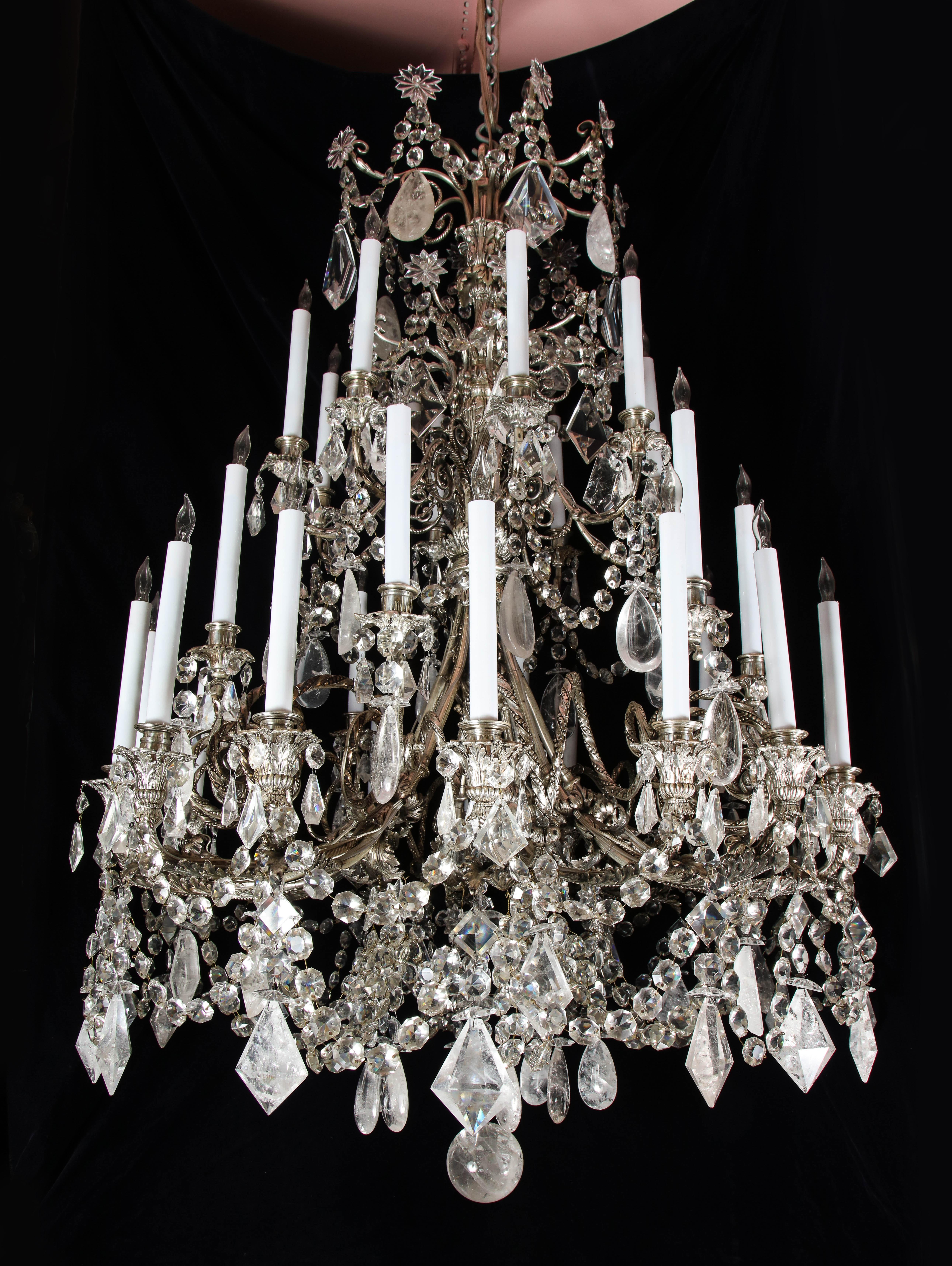 A spectacular and large antique French Louis XVI style silvered bronze, cut rock crystal and crystal 32 light triple tier chandelier of superb craftsmanship and unusual shape embellished with cut rock crystal prisms, cut crystal prisms and further
