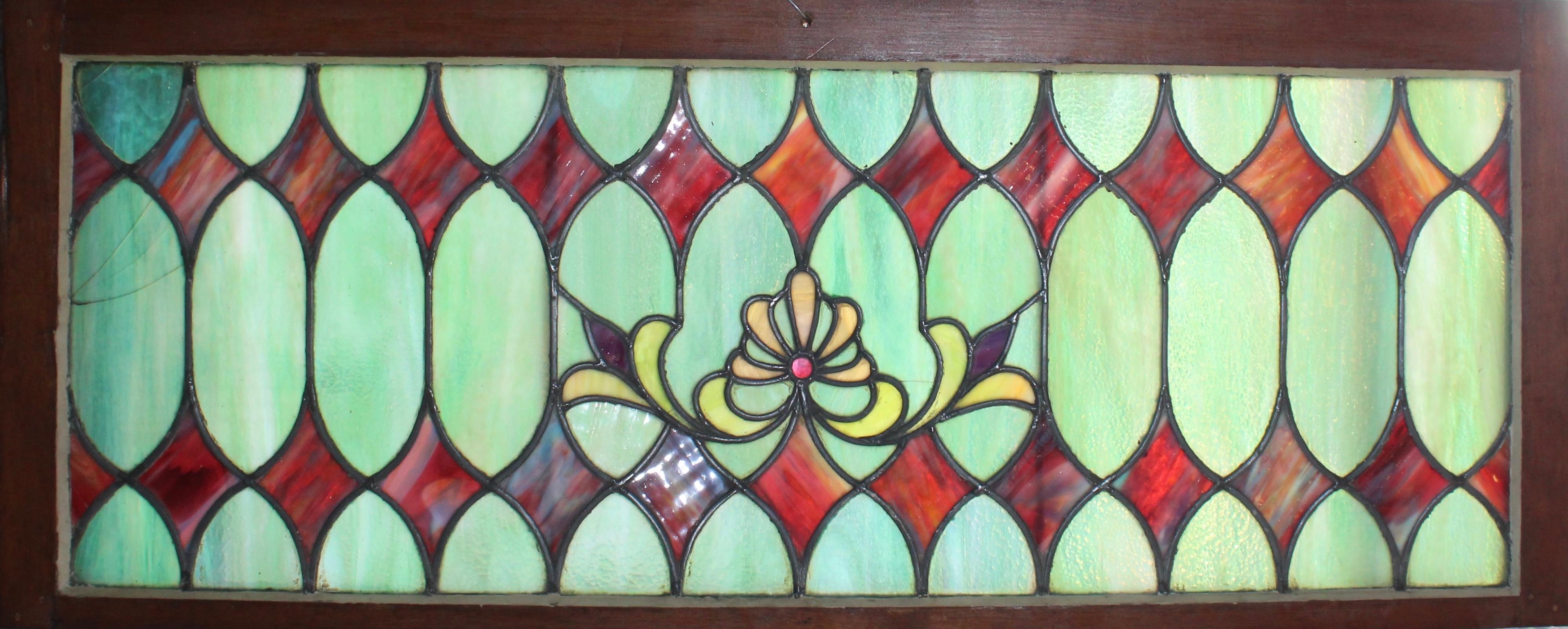 Esta ventana de 1,2 m de largo presenta vibrantes motivos de vidrieras para colocar encima de la puerta. Ricos diamantes púrpura entre dolores jaspeados azul turquesa. En el centro hay una flor de lis con una joya rosa.
Las dimensiones totales