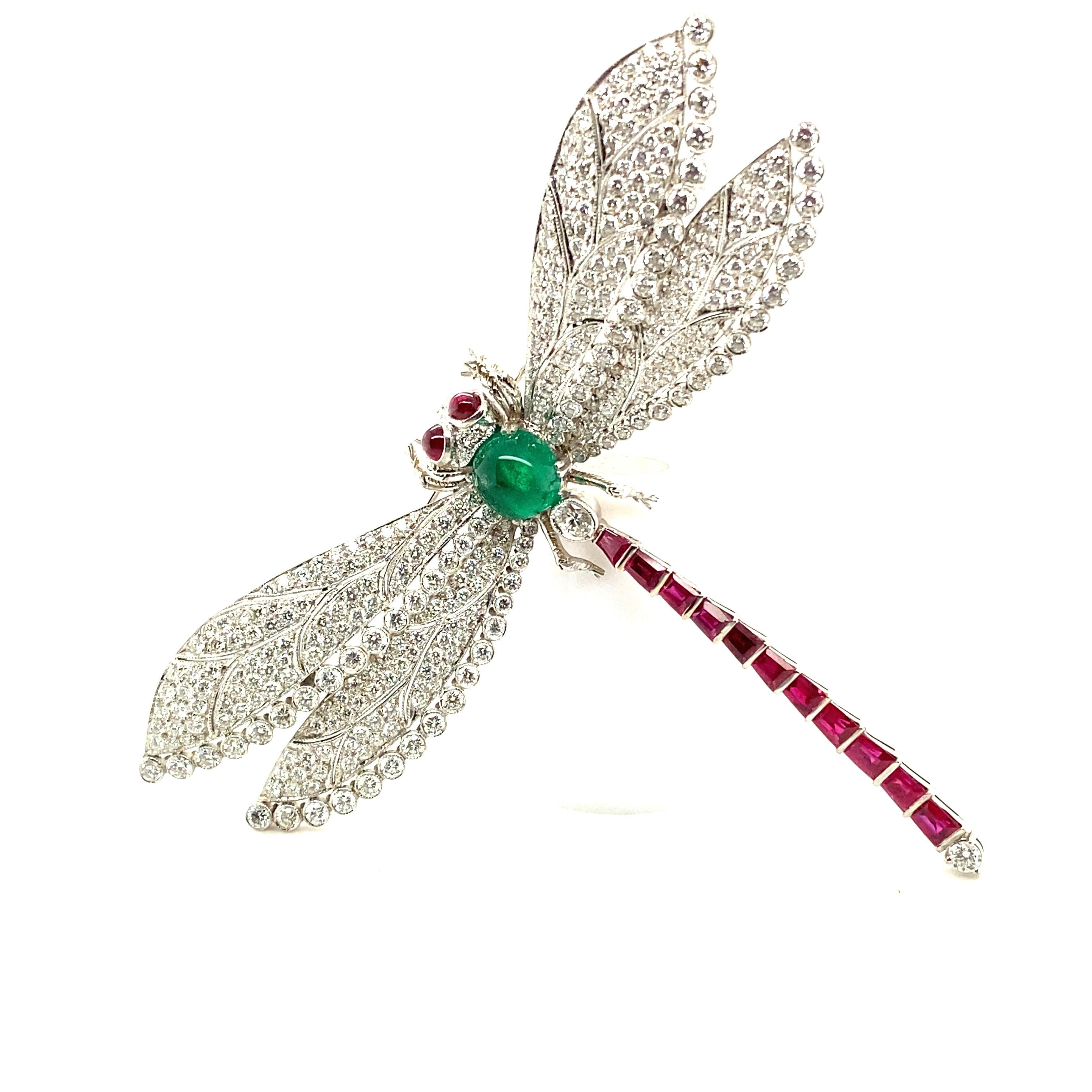 This spectacular and generously proportioned Art Deco style dragonfly brooch is crafted in 18 karat white gold and set with diamonds and vividly coloured gemstones.

The body is set with an emerald cabochon of approximately 2.90 carats and 13 round-