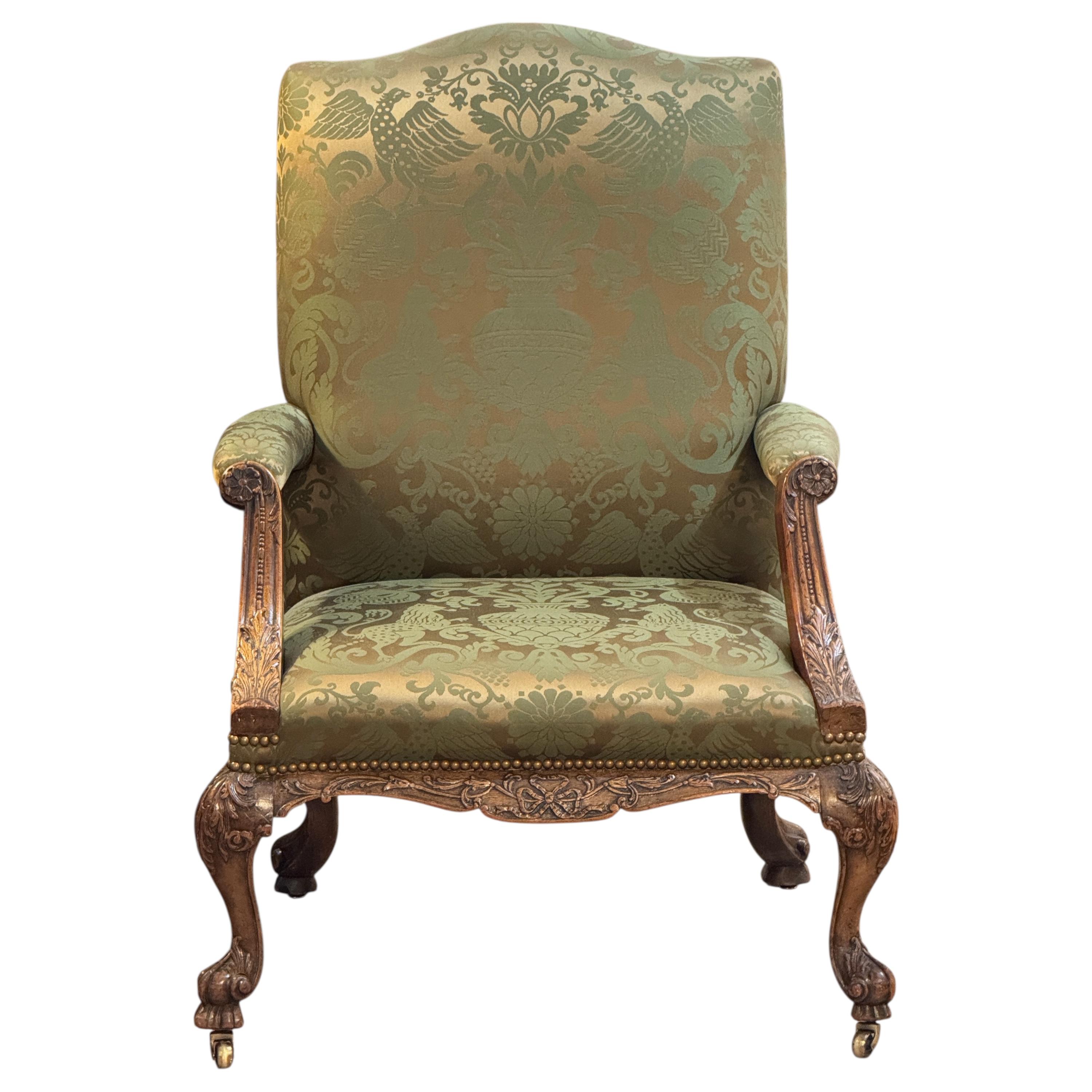 This mid-18th century library chair features deeply carved mahogany with acanthus motifs, scroll arms, and cabriole legs on casters. The rich green damask upholstery is finished with brass nailhead trim, highlighting the chair’s refined Georgian
