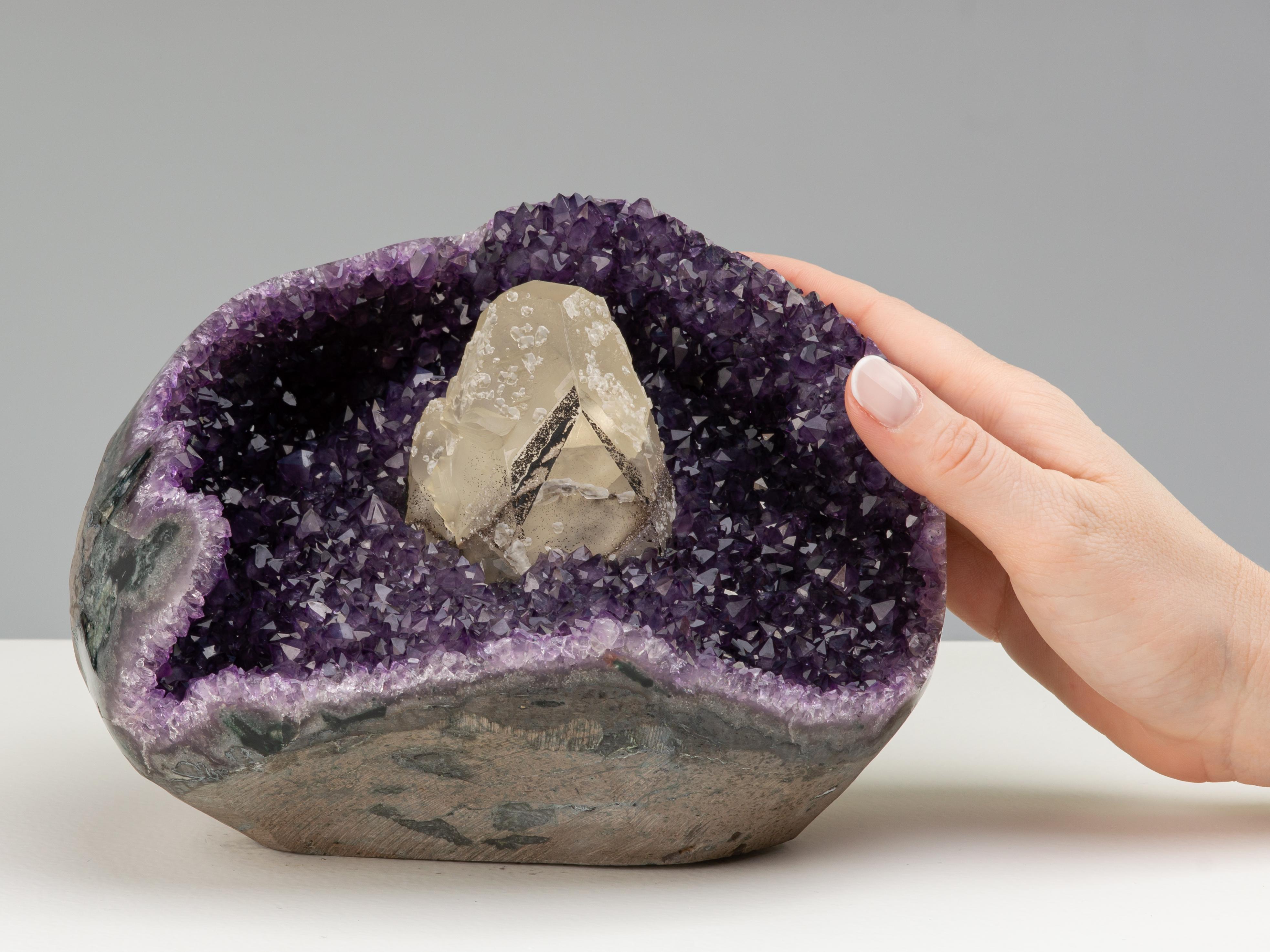 A stunning amethyst formation formed of a three quarter geode with cut window, revealing deep purple amethyst crystals, with a beautiful central calcite coated in black goethite and and white druzy quartz.

The piece is a wonderful example of the