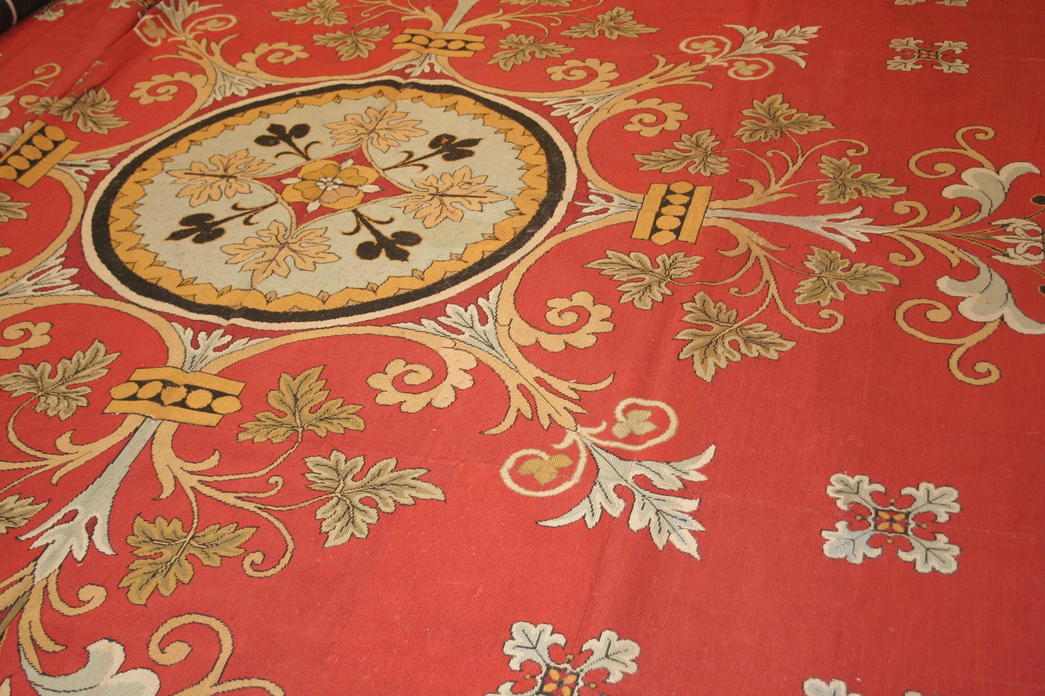 A stunning needlepoint carpet distinguished by a rich red field punctuated by a repeating floral motif and dominated by an impeccably executed central element, elegantly decorated with flowers and leafs placed on a roundel of neoclassical