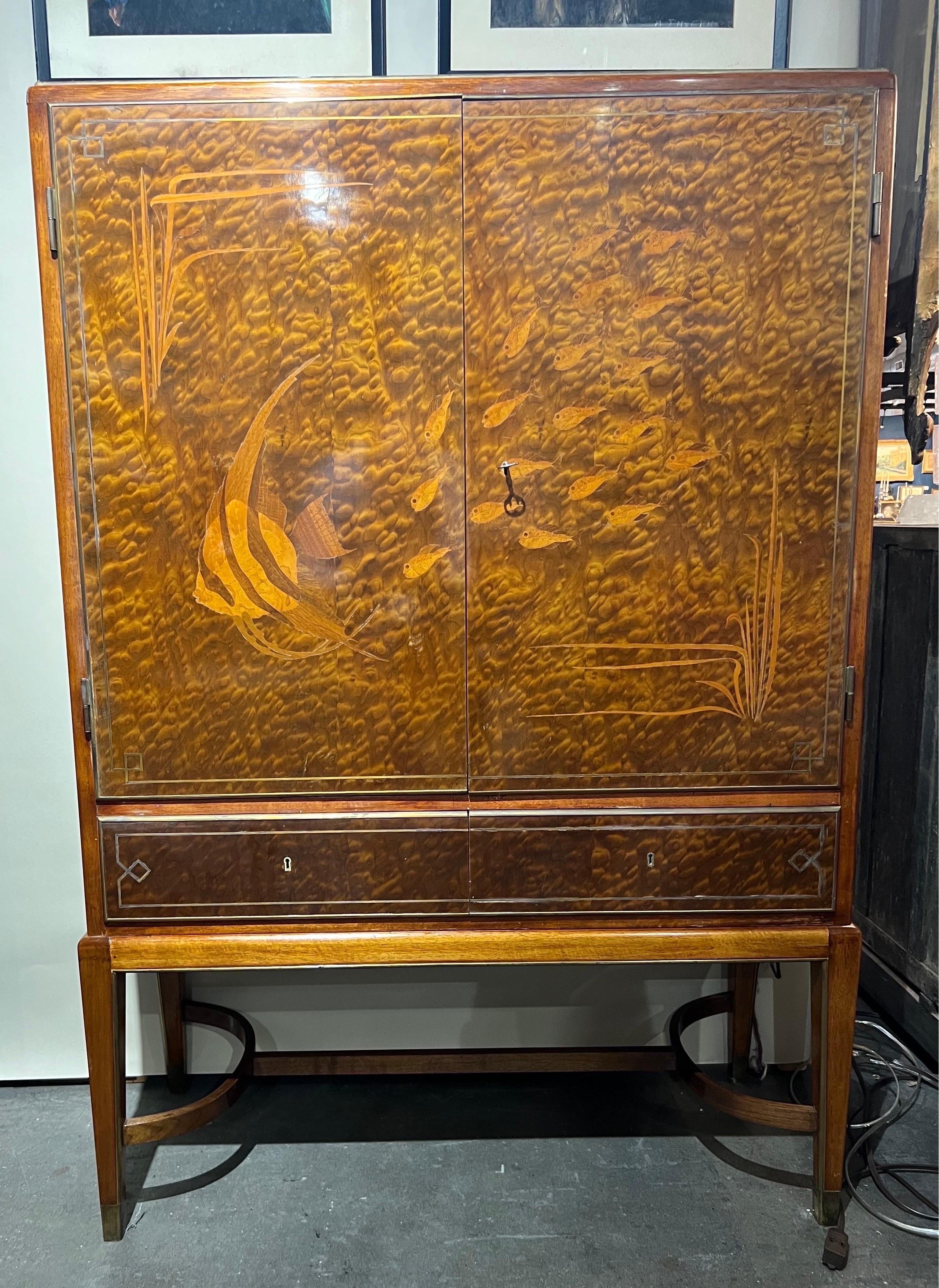Spectacular brass mounted fish inlaid art deco bar with two drawers. The individual fish and seaweed are inlaid and made of an exotic hardwood. The background is a HIGHLY figured exotic hardwood that is cut in a way to resemble water. The interior