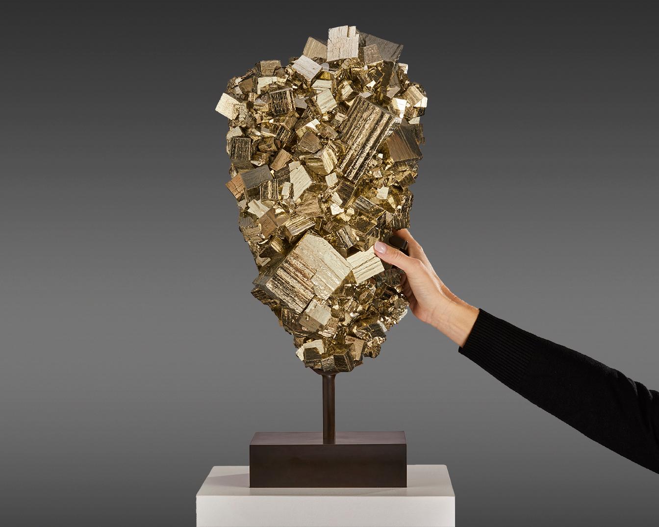 Impressive sculpture features a large cluster of Pyrite,
masterfully extracted from the depths of Peru. Renowned
for its metallic luster and golden hue, Pyrite—often called
“Fool’s Gold”—creates a captivating visual symphony of cubes
varying in