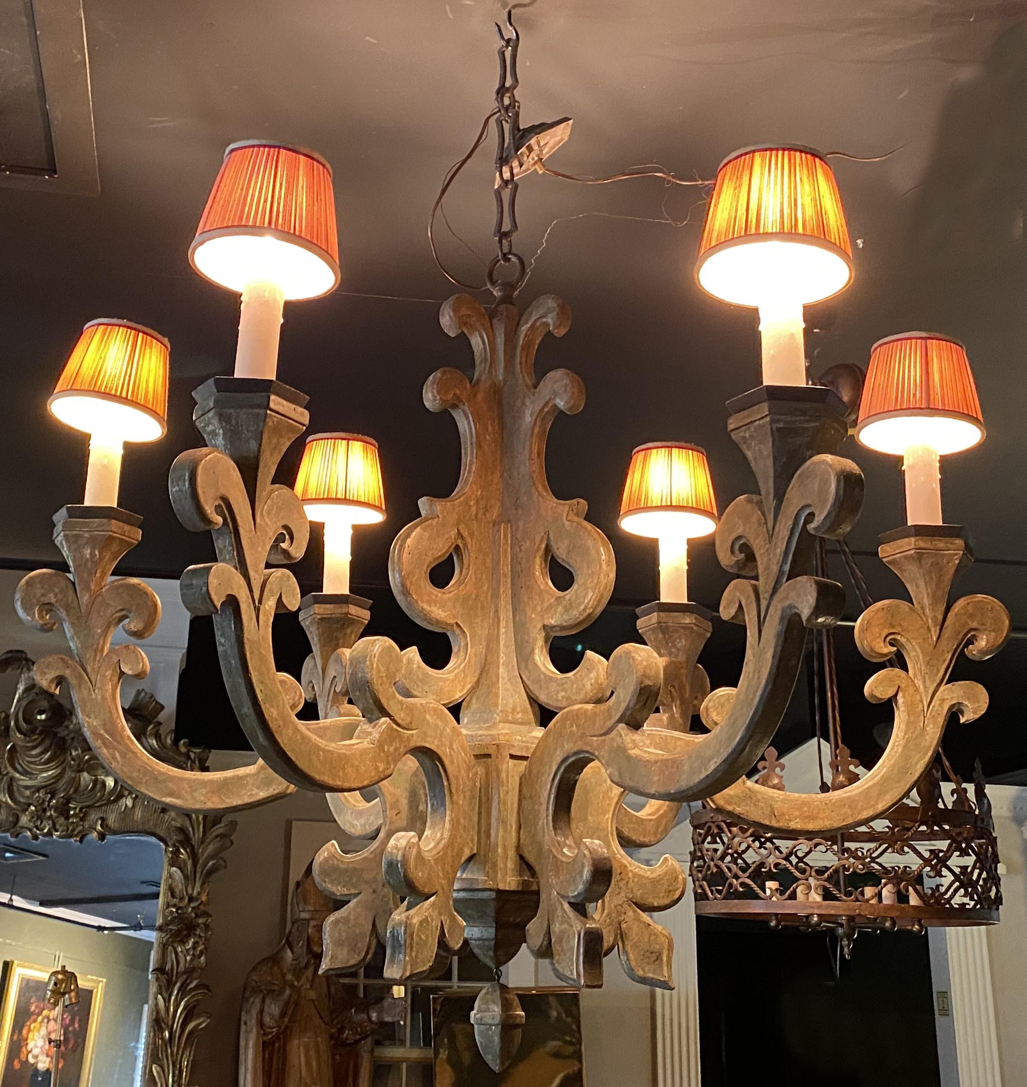 A wonderful wooden six light chandelier by Jerry Pair with scroll carved arms , beeswax candle sleeves and lamp shades, and includes hexagonal metal canopy and chain, and acorn form drop finial, referred to as the Lyon chandelier. Since 1970, Jerry