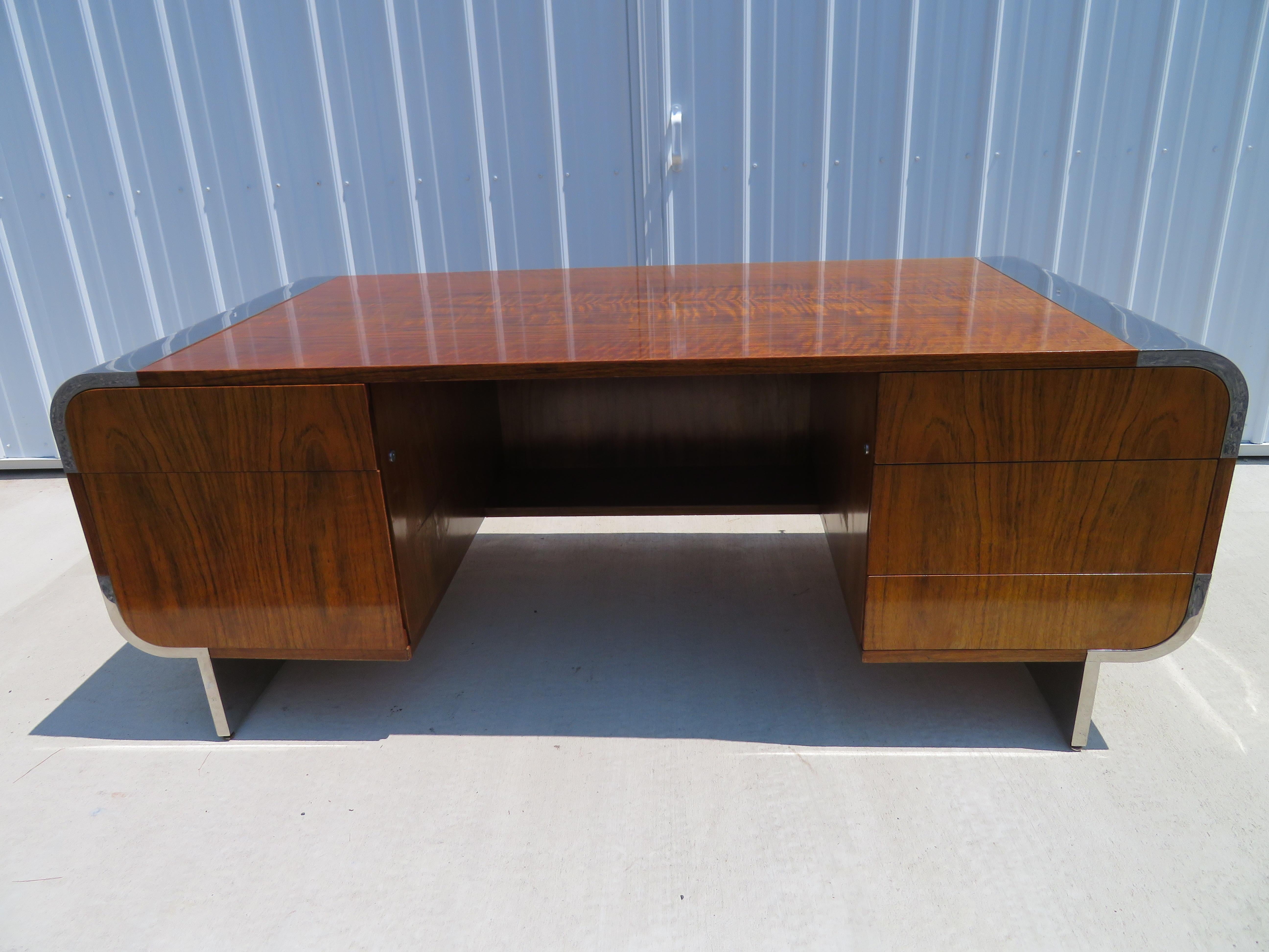 Stunning burled walnut and stainless steel desk by Pace, designed by Irving Rosen. Waterfall edges with polished stainless steel. 3 drawers flank the right side and 2 drawers flank the left side, including a large file drawer. Working lock with