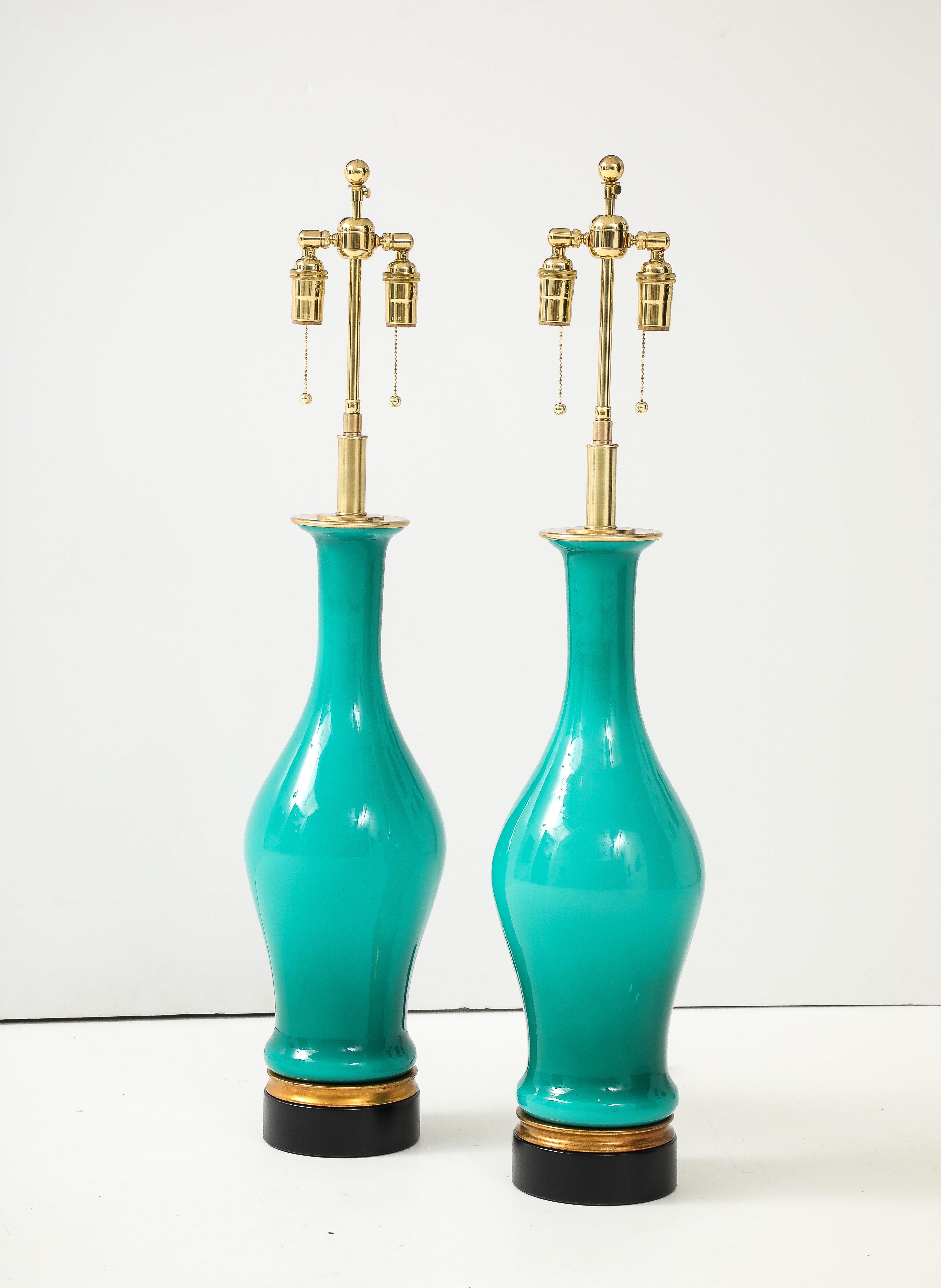 Spectaculaire paire de grandes lampes en verre de Murano dans une  Rare couleur Aqua étonnante.
Les corps de lampe en verre reposent sur des bases noires et dorées.
Les lampes ont été refaites à neuf avec des doubles grappes réglables en laiton poli