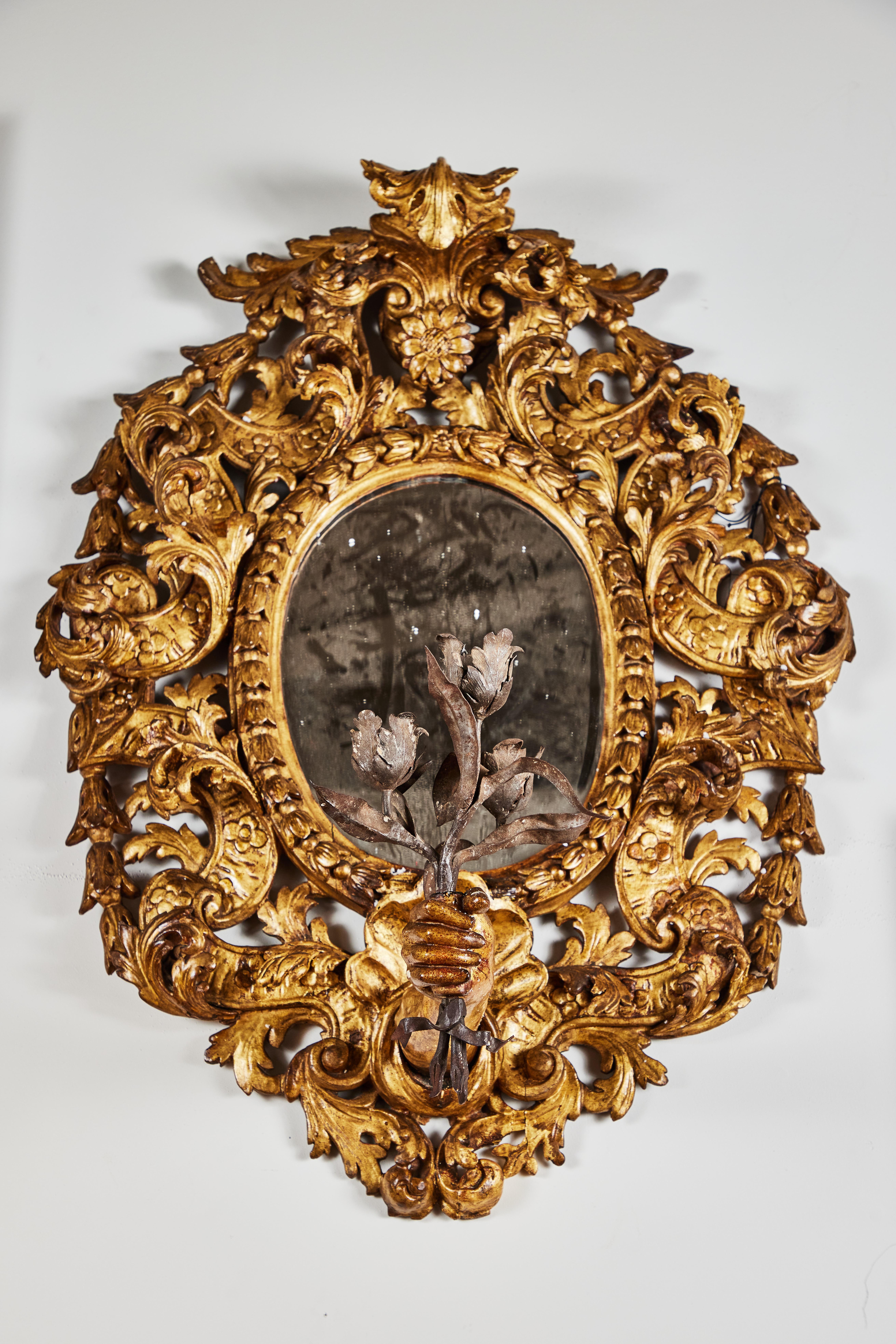 A rare and unusual pair of circa 1850, hand carved, gessoed, and 22-karat gold gilded pierced wood frames with an elaborate array of foliate scrolls surmounted by a curled acanthus leaf. The bottom of each featuring remarkable, thrusting forearms