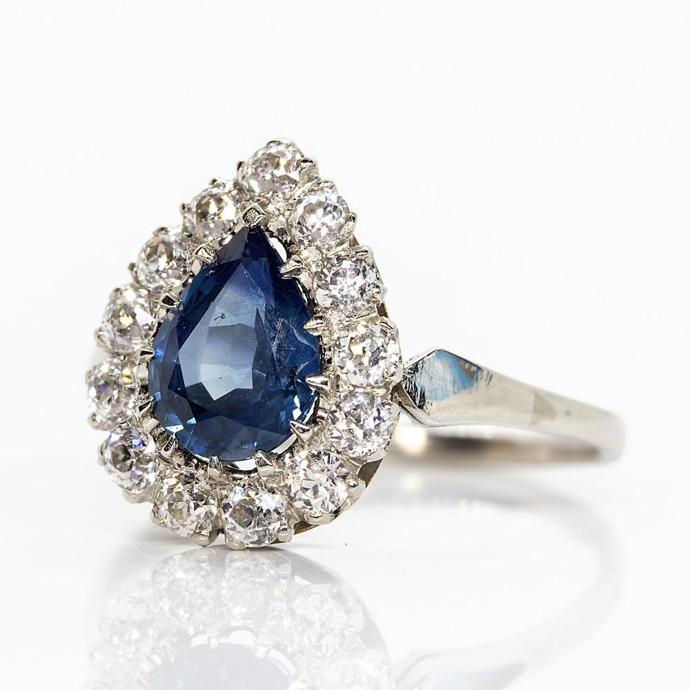 This enticing piece of jewelry features a prominent natural pear shape sapphire that weighs 1.40ctw.
The central gemstone is surrounded by a row of 13 glowing old mine cut diamonds of H-VS2 quality that weigh 0.50ctw.
This lovely ring was handmade