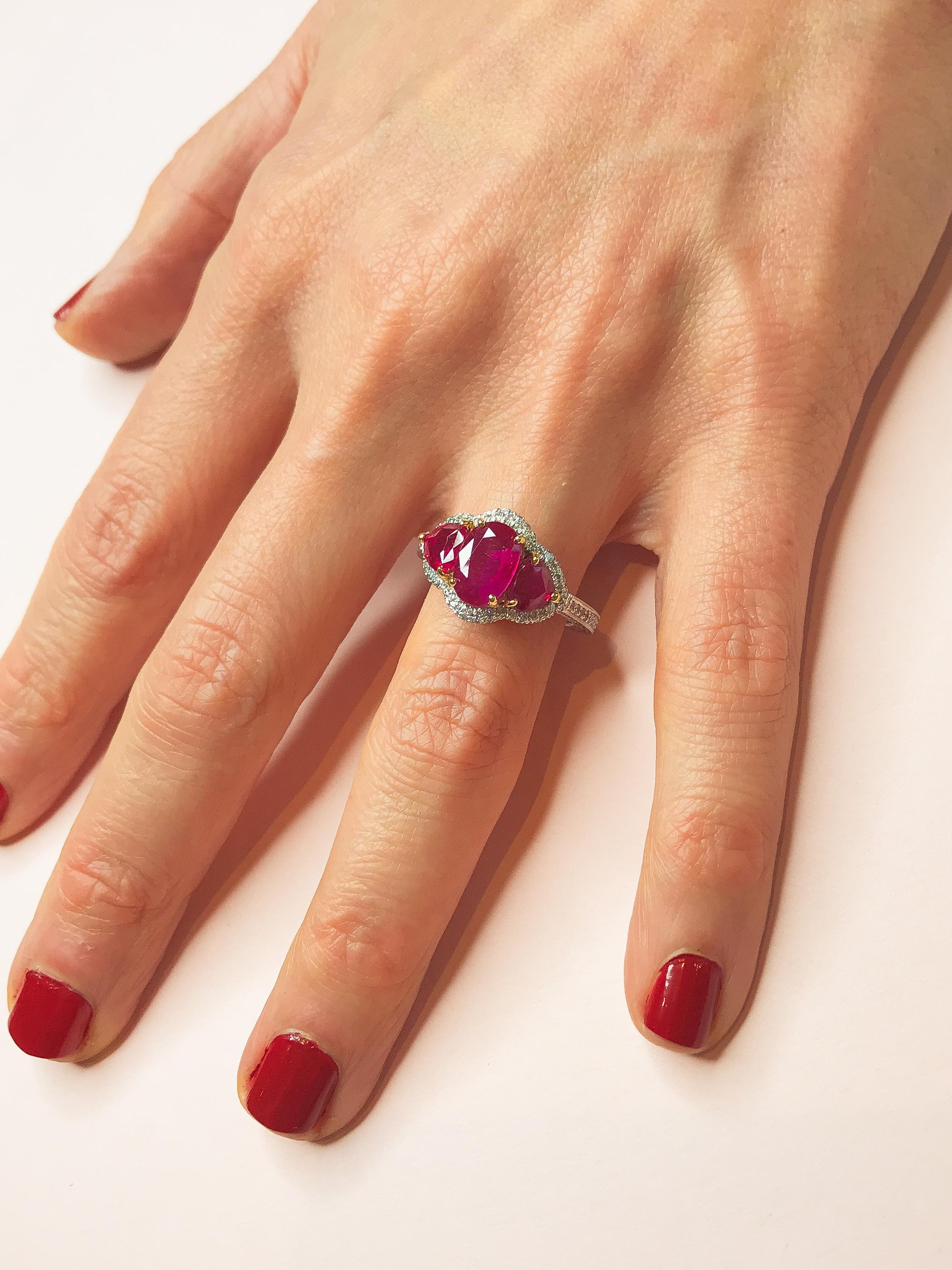 A three-stone ring like no other, this exquisite piece features an enticing pinkish red ruby in a timeless oval shape and two smaller, trilliant cut rubies in the same arresting colour. The stones are set in yellow gold and embraced by a dazzling
