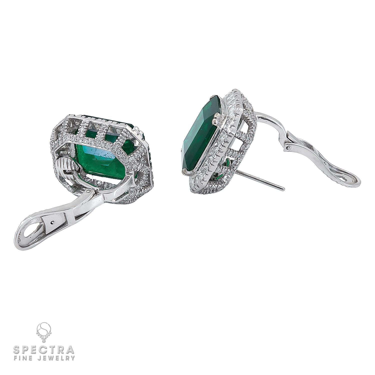 This pair of Art Deco-inspired geometric emerald and diamond pierced earrings with French clips are made by Spectra Fine Jewelry in the contemporary era, circa 2010s, and feature two emerald-cut green emeralds, weighing approximately 23.44 carats